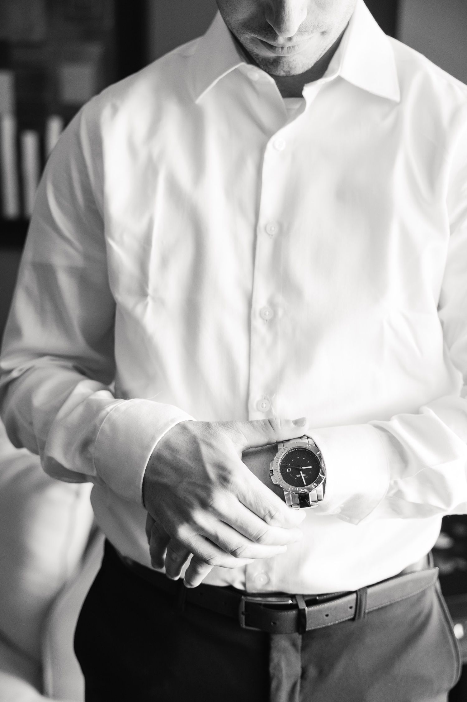 Close-up of man in white dress shirt adjusting watch while getting ready.