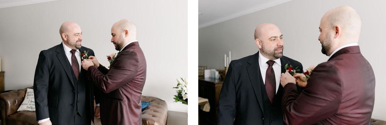 Two people helping each other with boutonnieres while wearing dark suits.