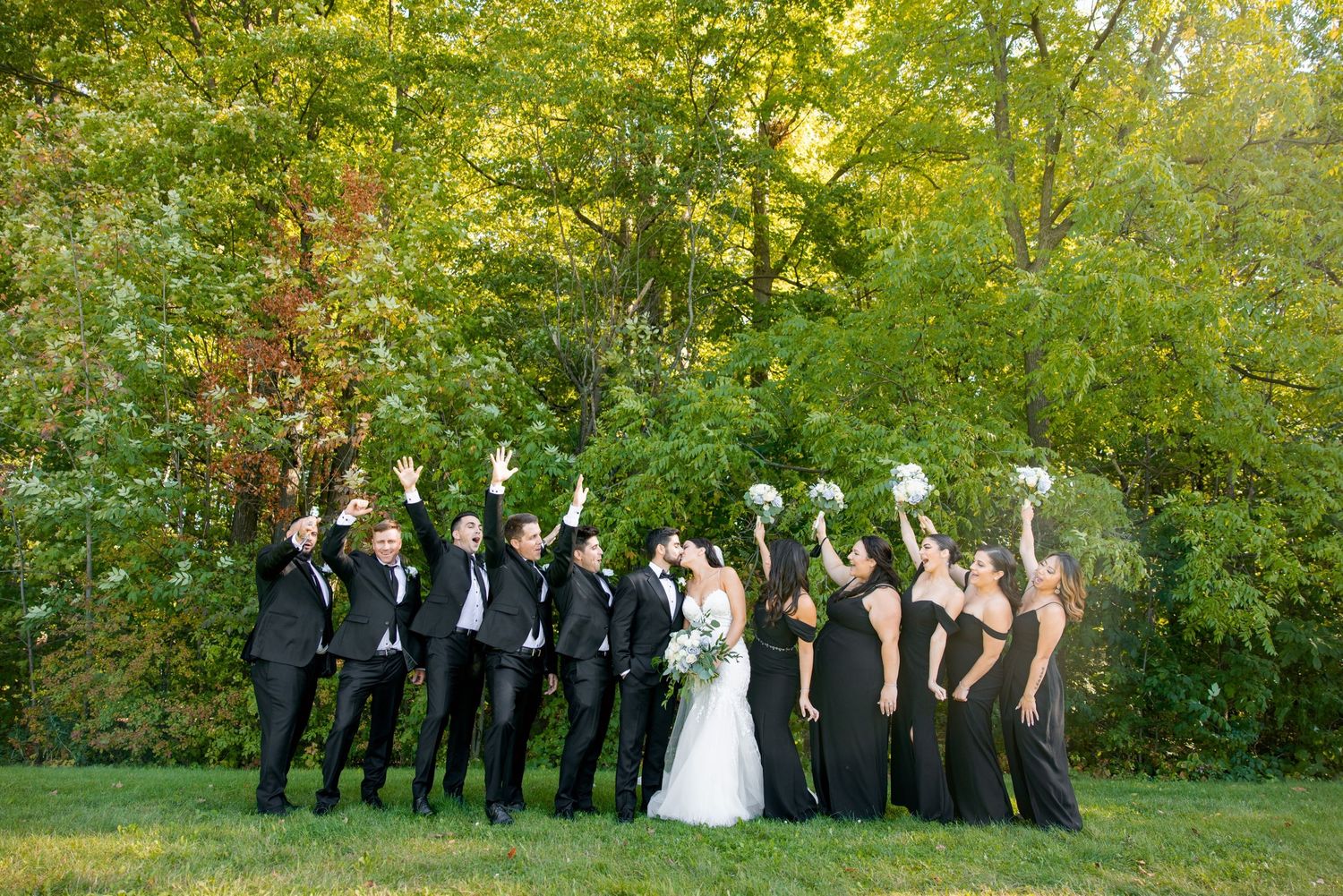 Wedding party strikes a fun pose outdoors with bridesmaids in black dresses.