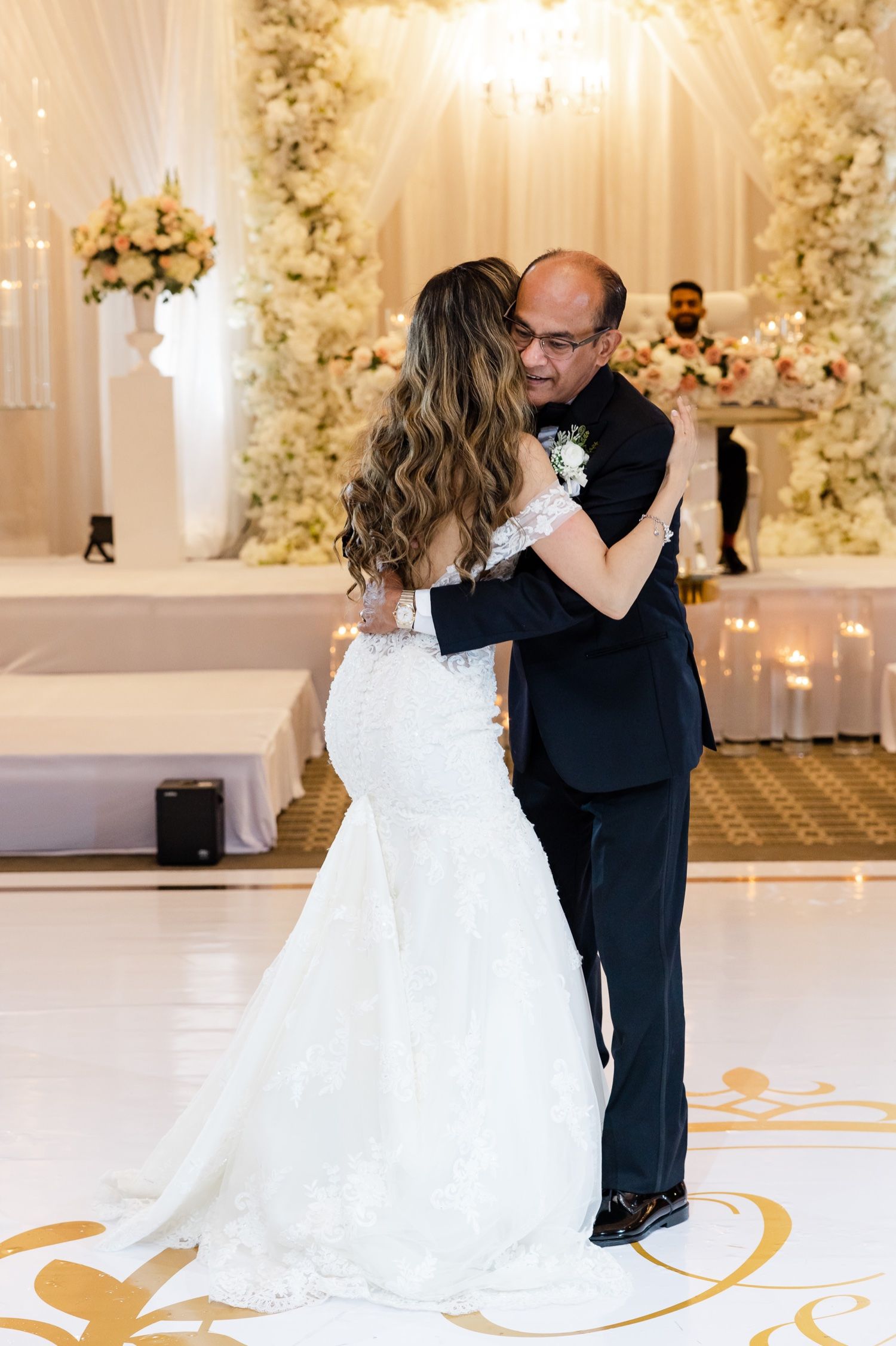 Couple embraces during emotional wedding dance in elegant venue with floral backdrop.