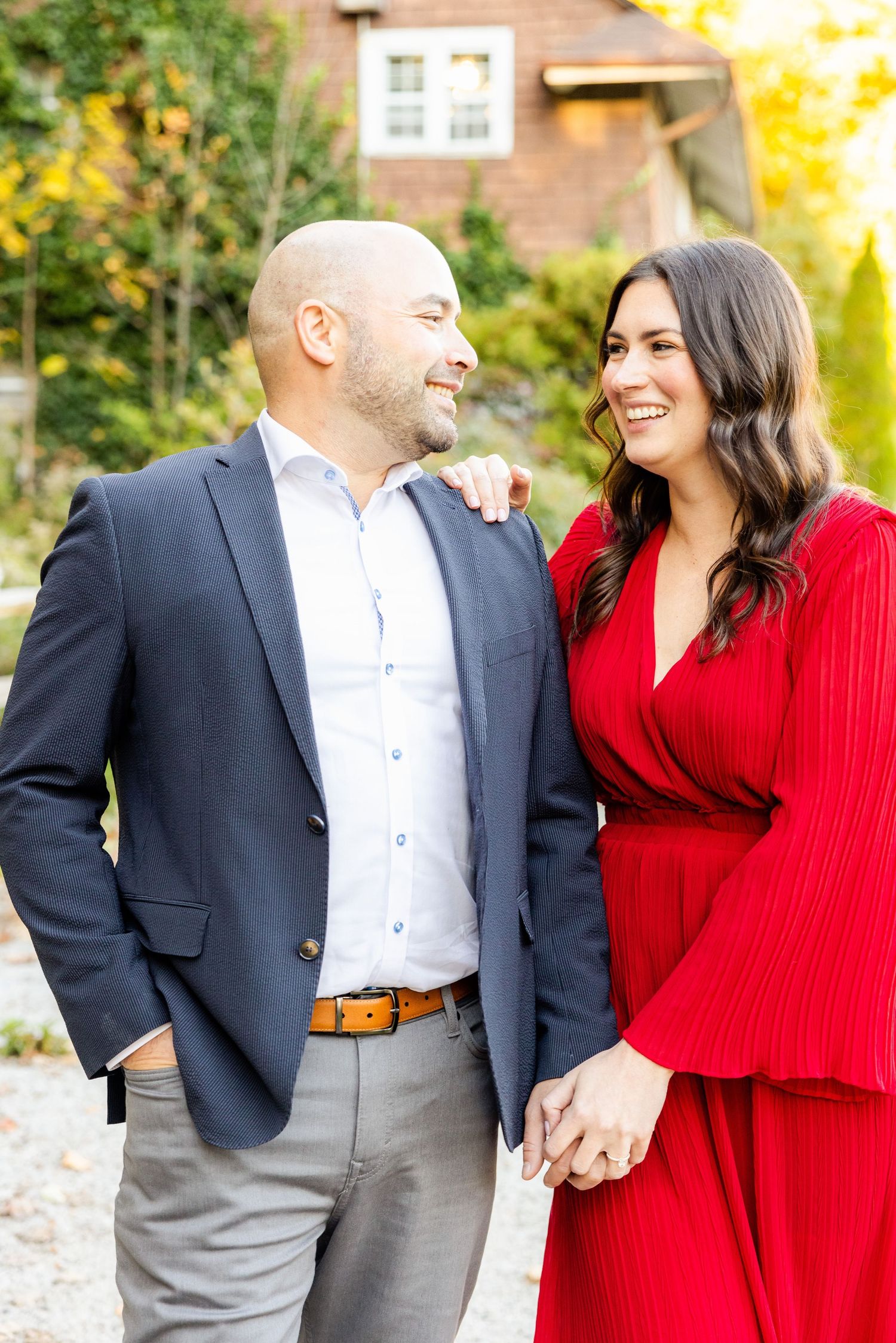 Couple shares genuine laughter during outdoor portrait session in contrasting formal attire.