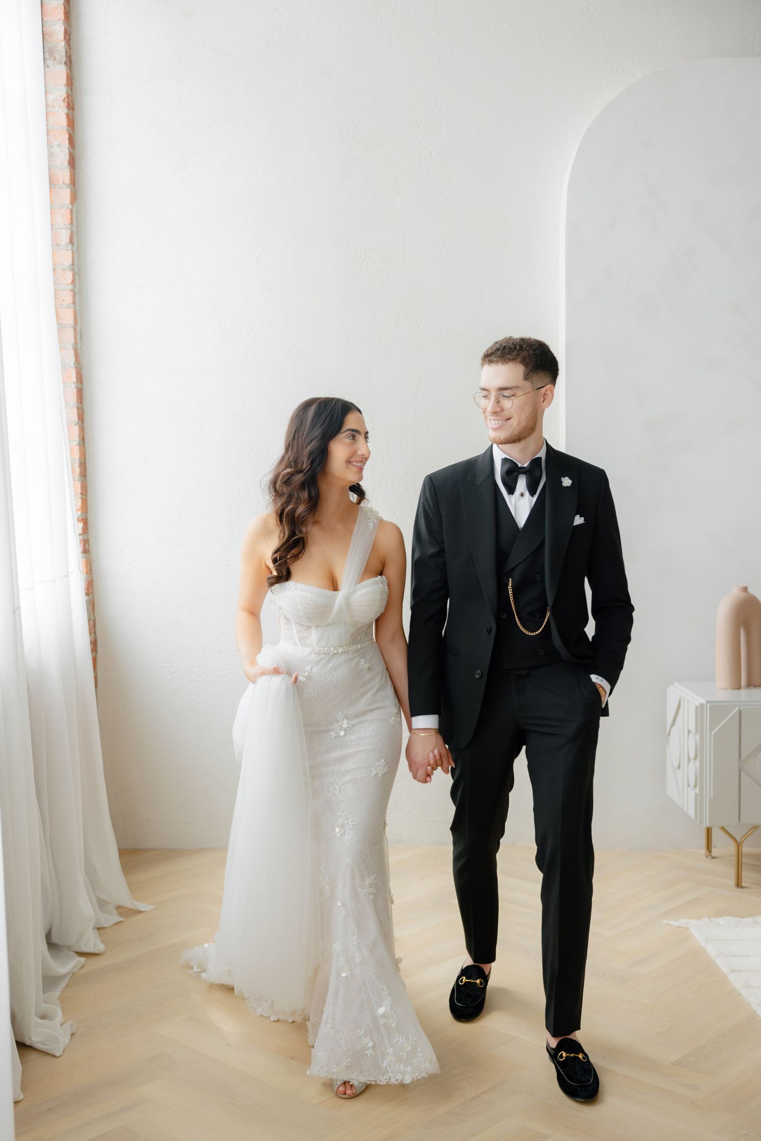 Romantic wedding couple walking together in a bright minimalist room with natural light.