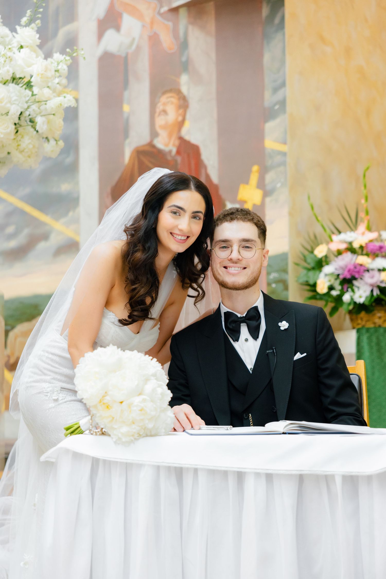 A couple signs their marriage certificate at a decorated table with white flowers.