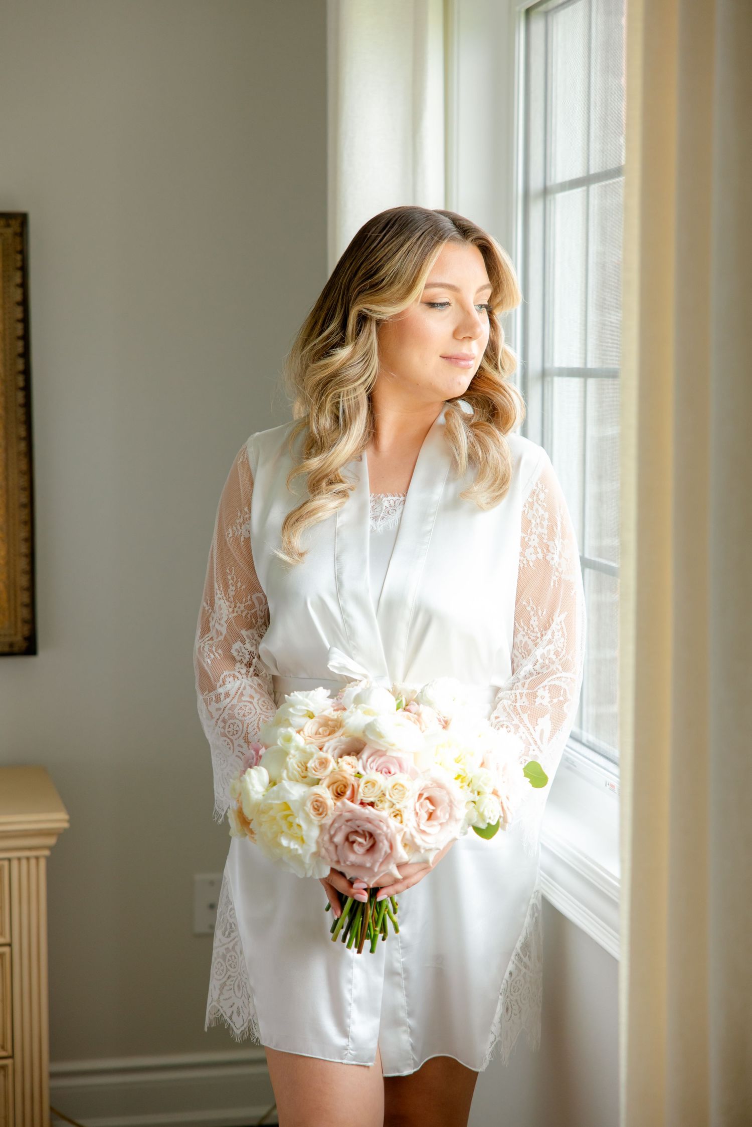 Bridal preparation with soft pink and white rose bouquet by bright window.