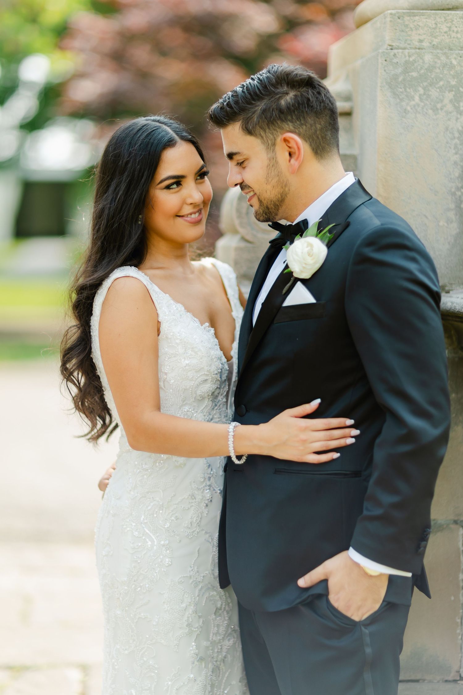 Sunlit wedding portrait of couple in formal attire sharing loving moment in garden setting.