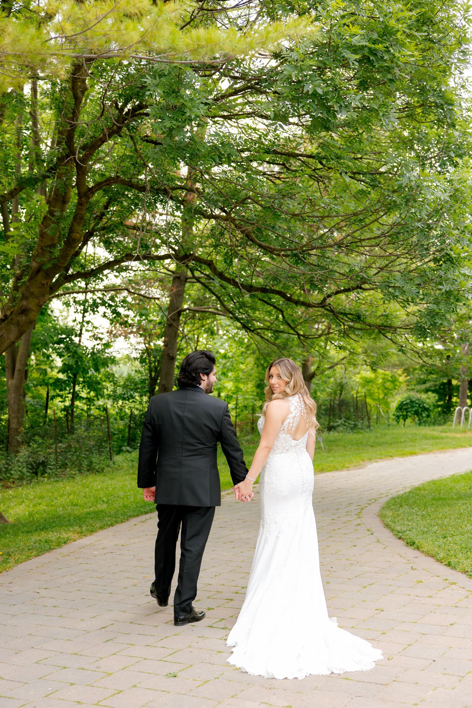 A bride and groom holding hands while walking away on a winding garden pathway.