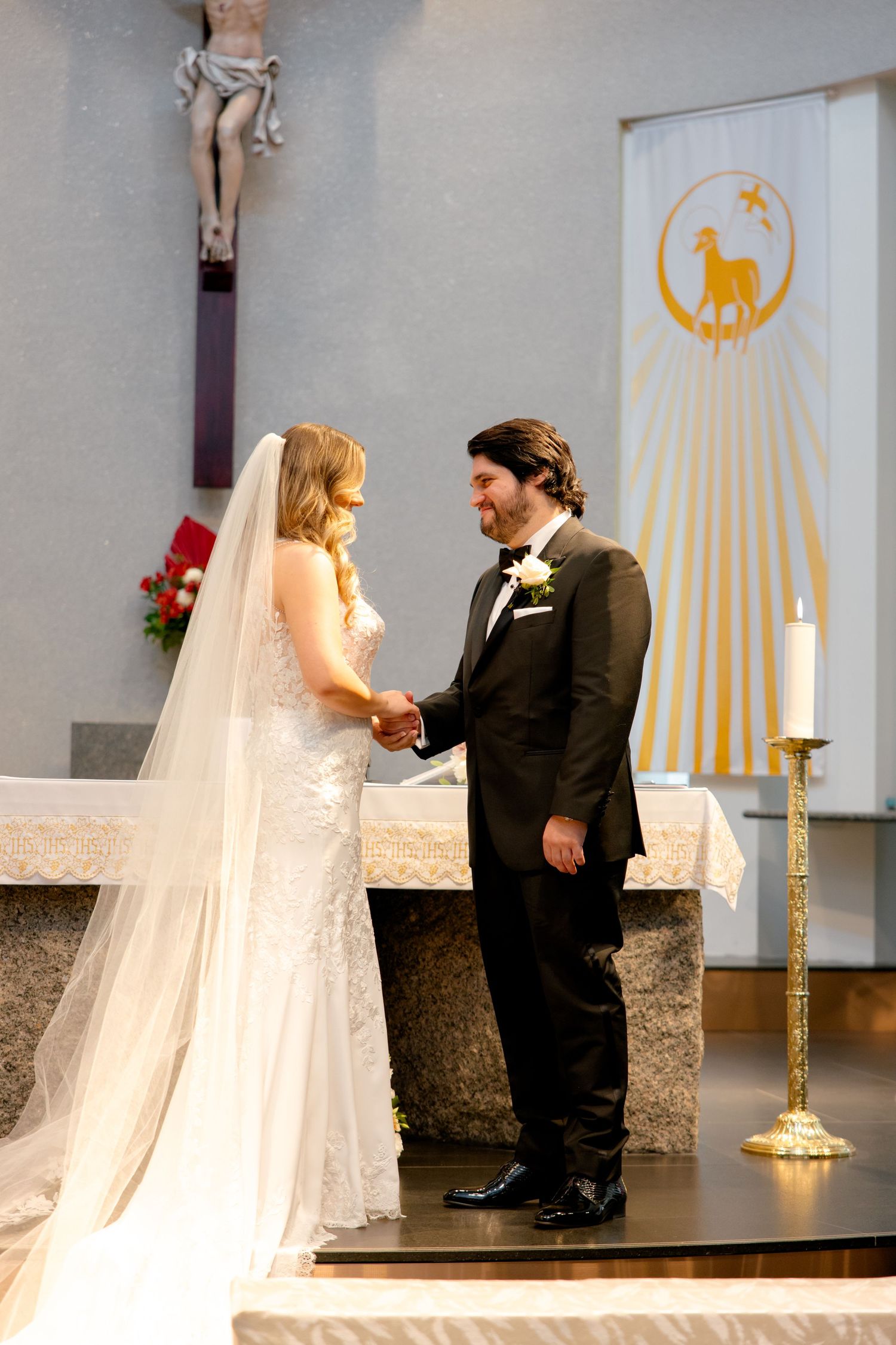 Couple exchanging vows at church altar with crucifix and decorative banners in background.