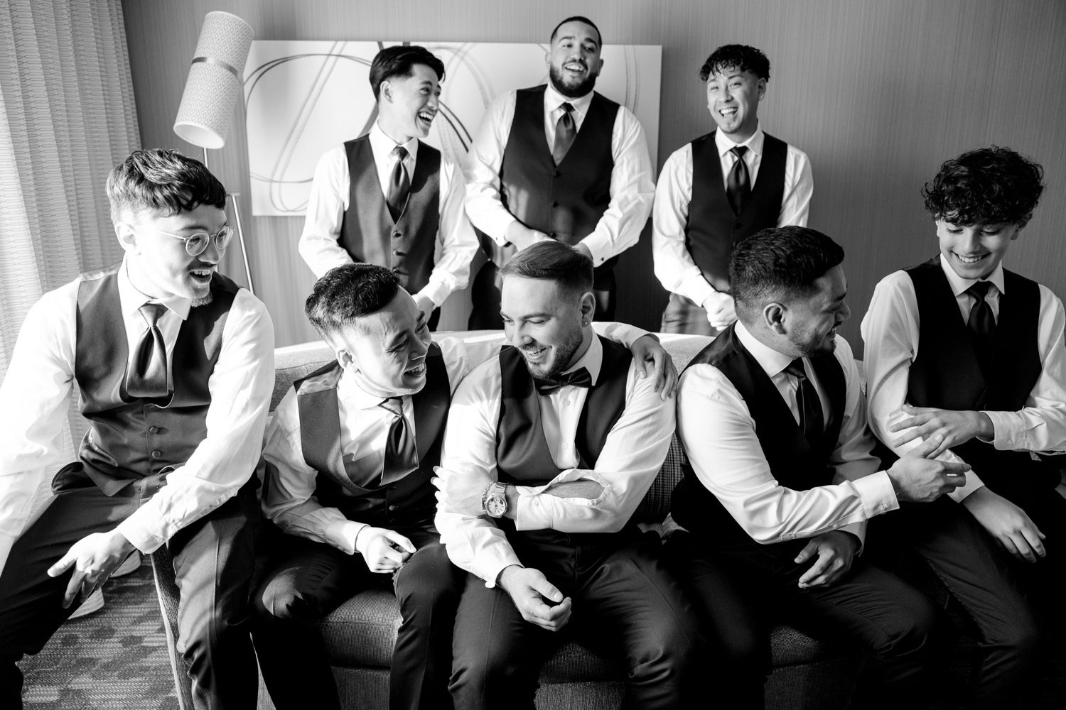 Groomsmen in matching navy vests and white shirts pose together on a couch.