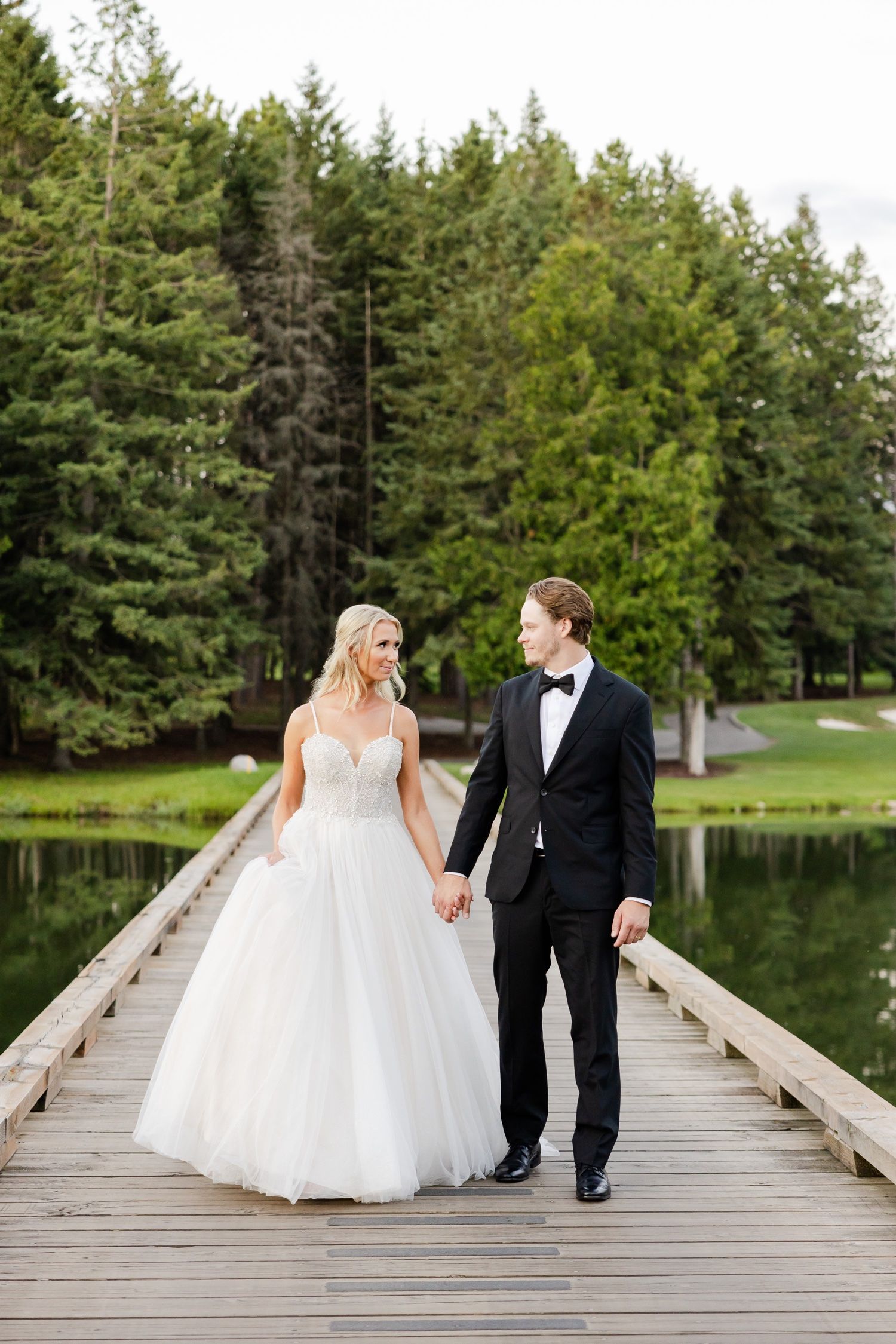Couple sharing intimate moment while walking on wooden bridge by serene pond.