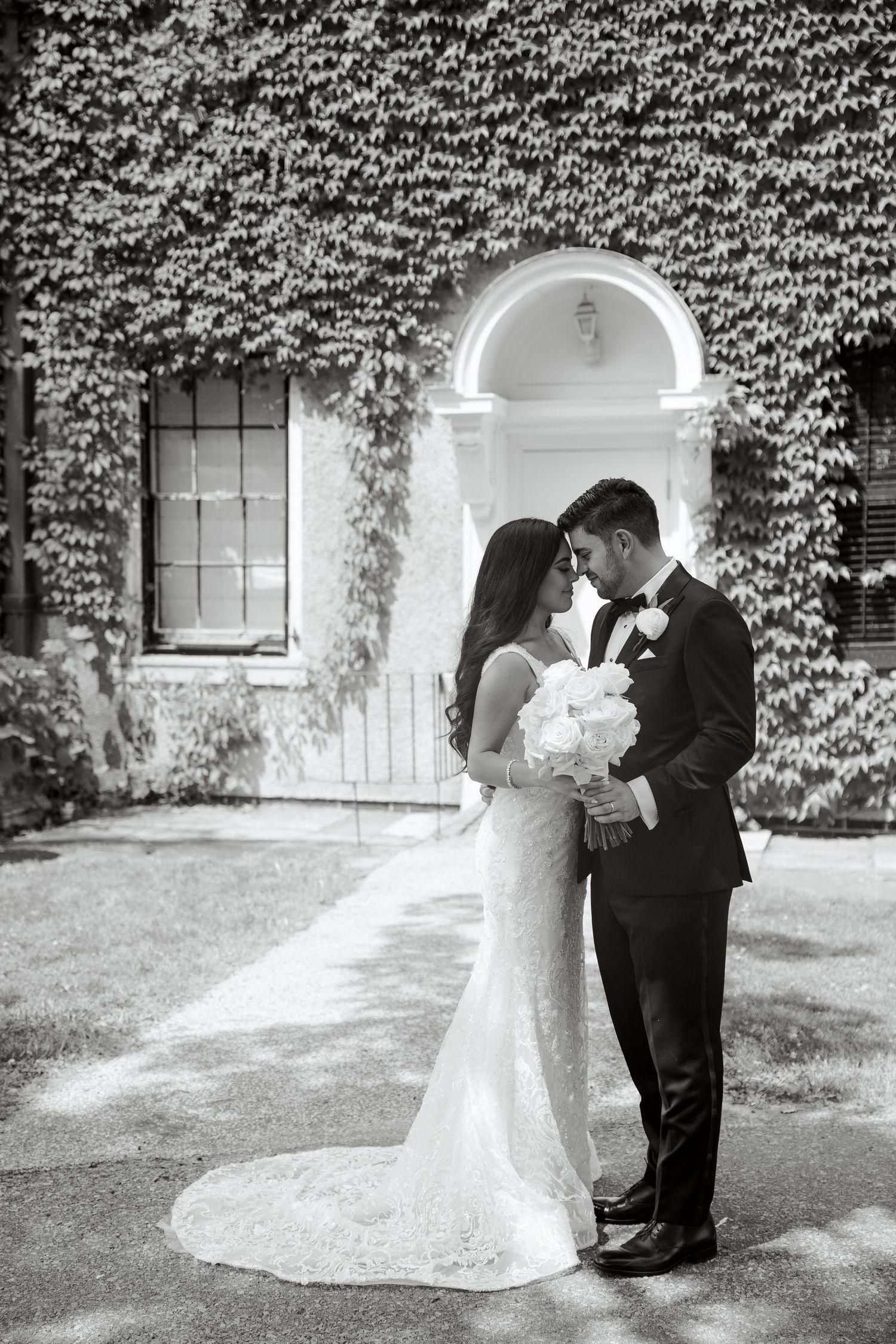 Black and white wedding photo capturing a tender moment in front of an ivy-covered entrance.