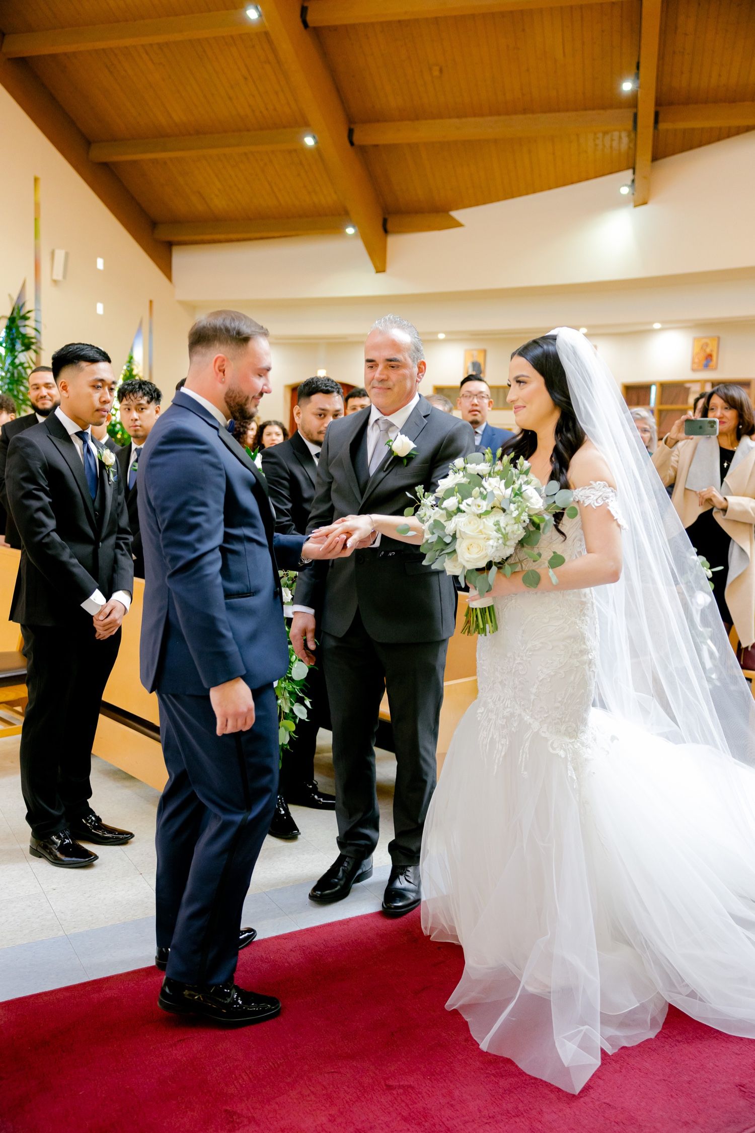 Traditional wedding ceremony in progress at an elegant church with wood beam ceilings and red carpet.