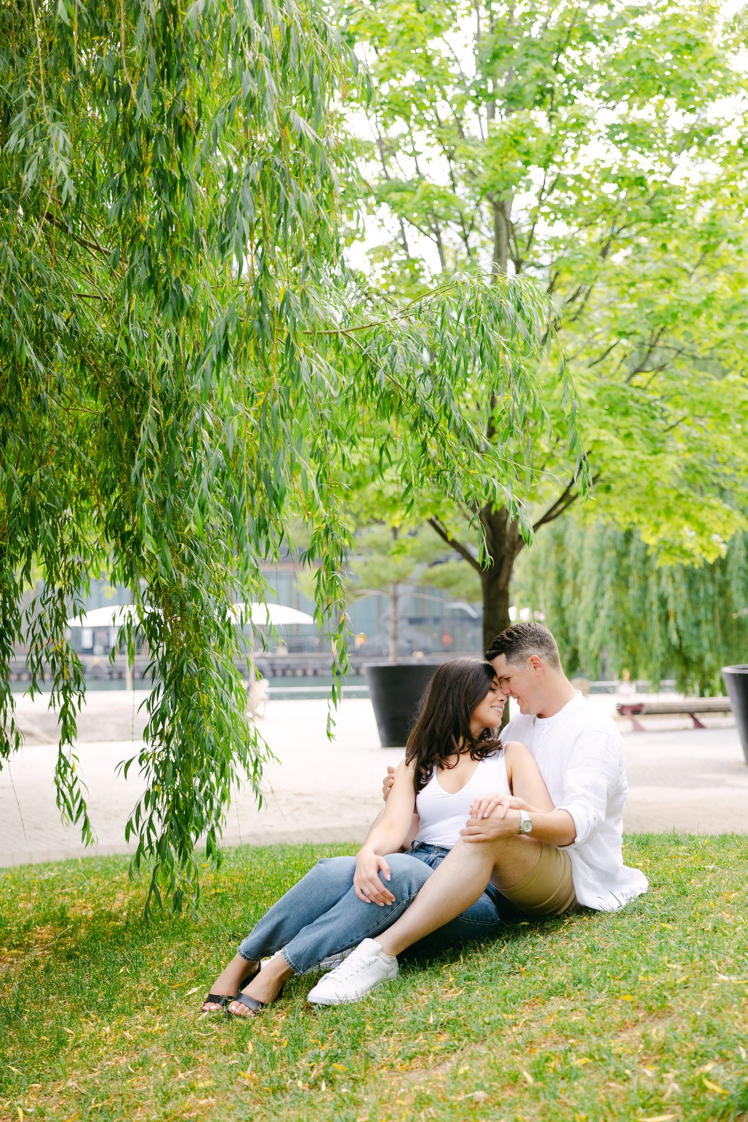 Intimate couple moment captured under swaying willow trees in park setting.