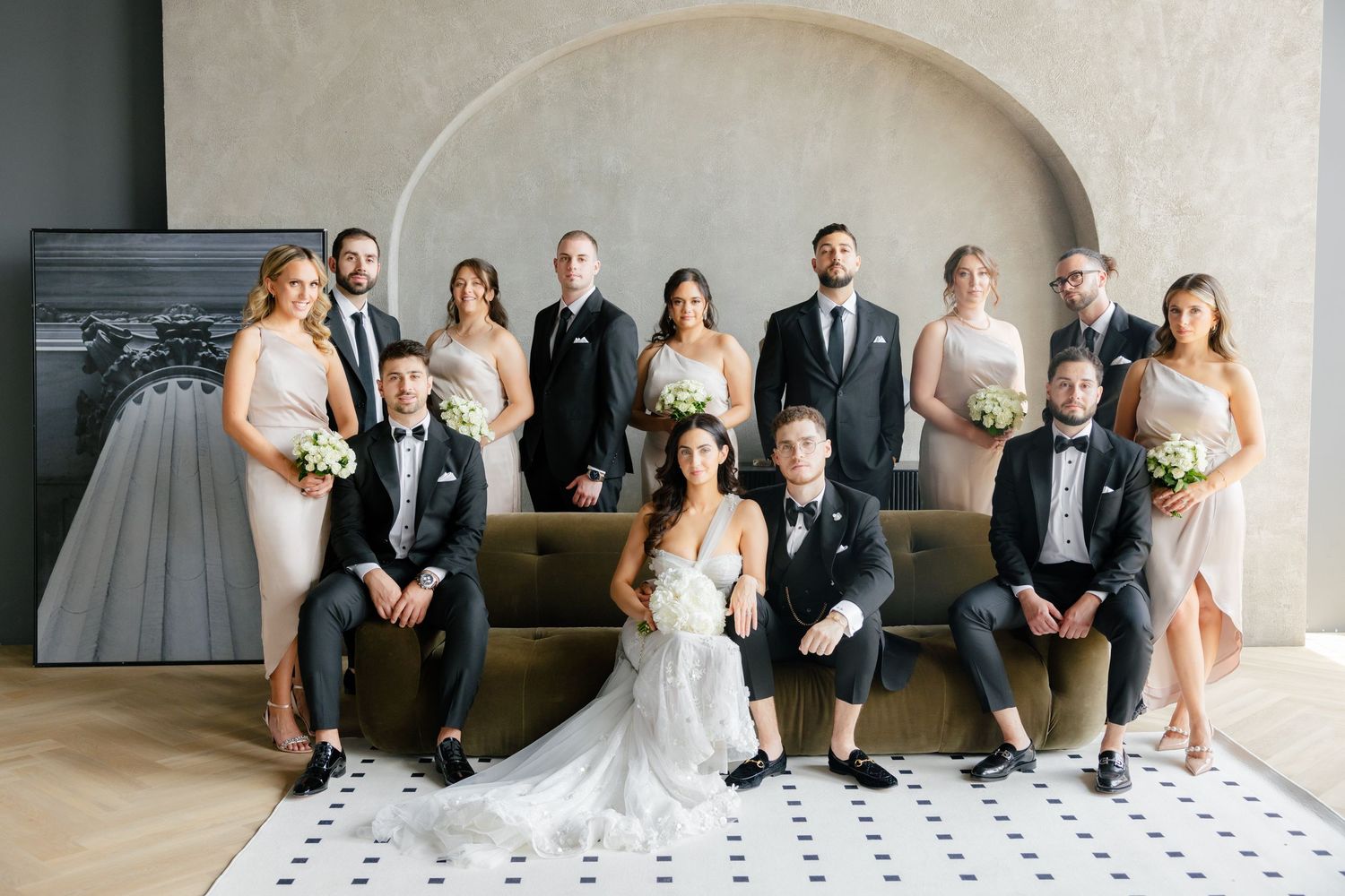 Elegant wedding party group photo featuring formal attire against a modern minimal backdrop.