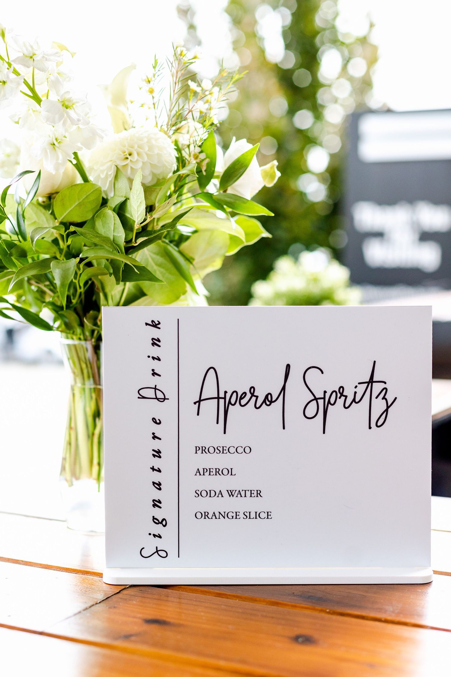 Aperol Spritz cocktail menu card displayed with white floral arrangement.
