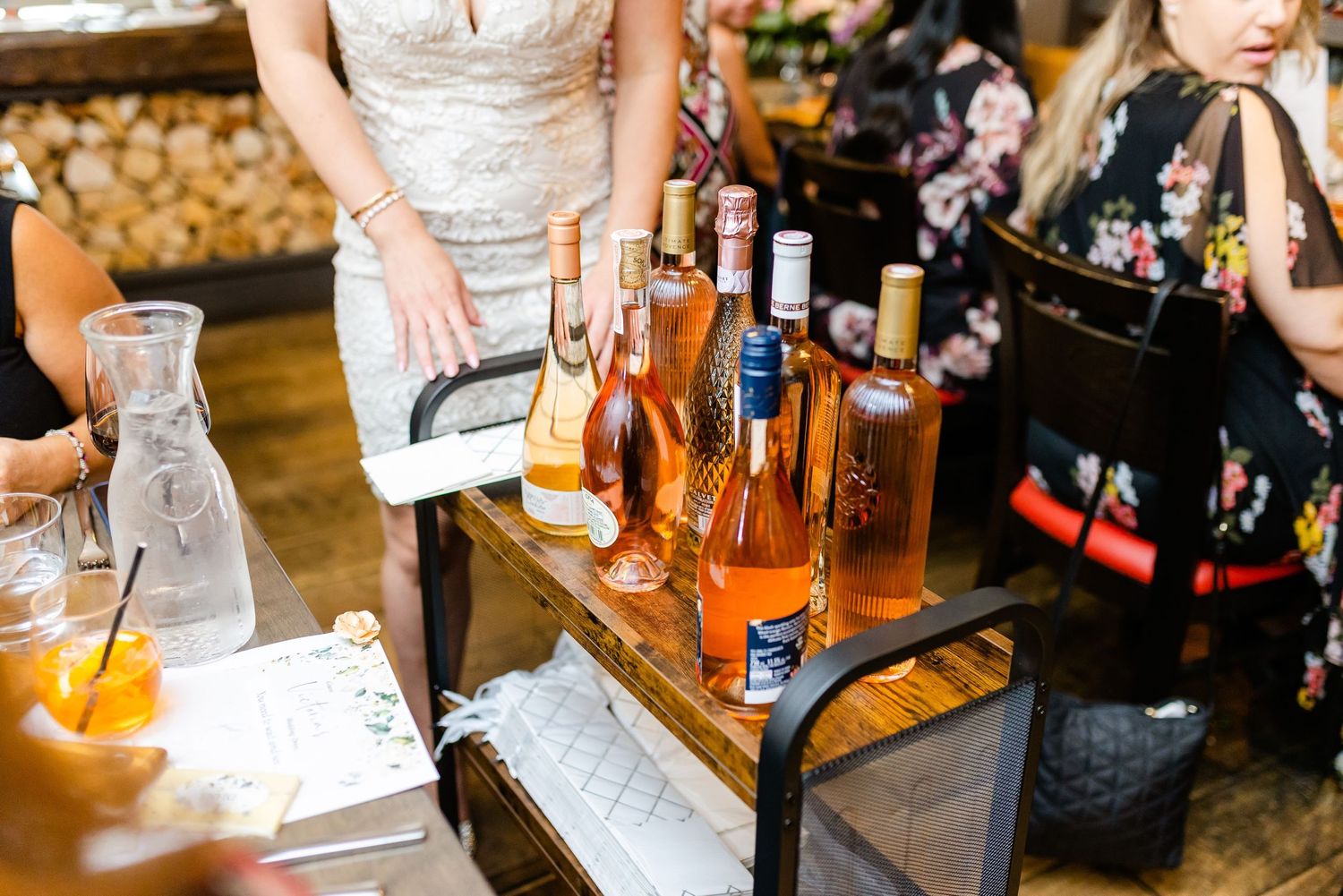 Wine bottles and cocktail ingredients arranged on a wooden bar cart at an event.