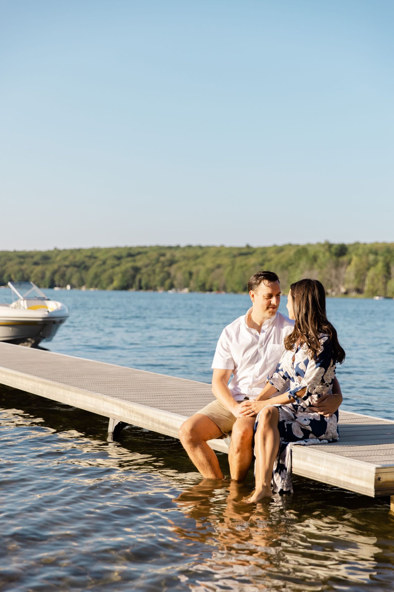 A couple shares an intimate moment while sitting on a wooden dock over a calm lake.