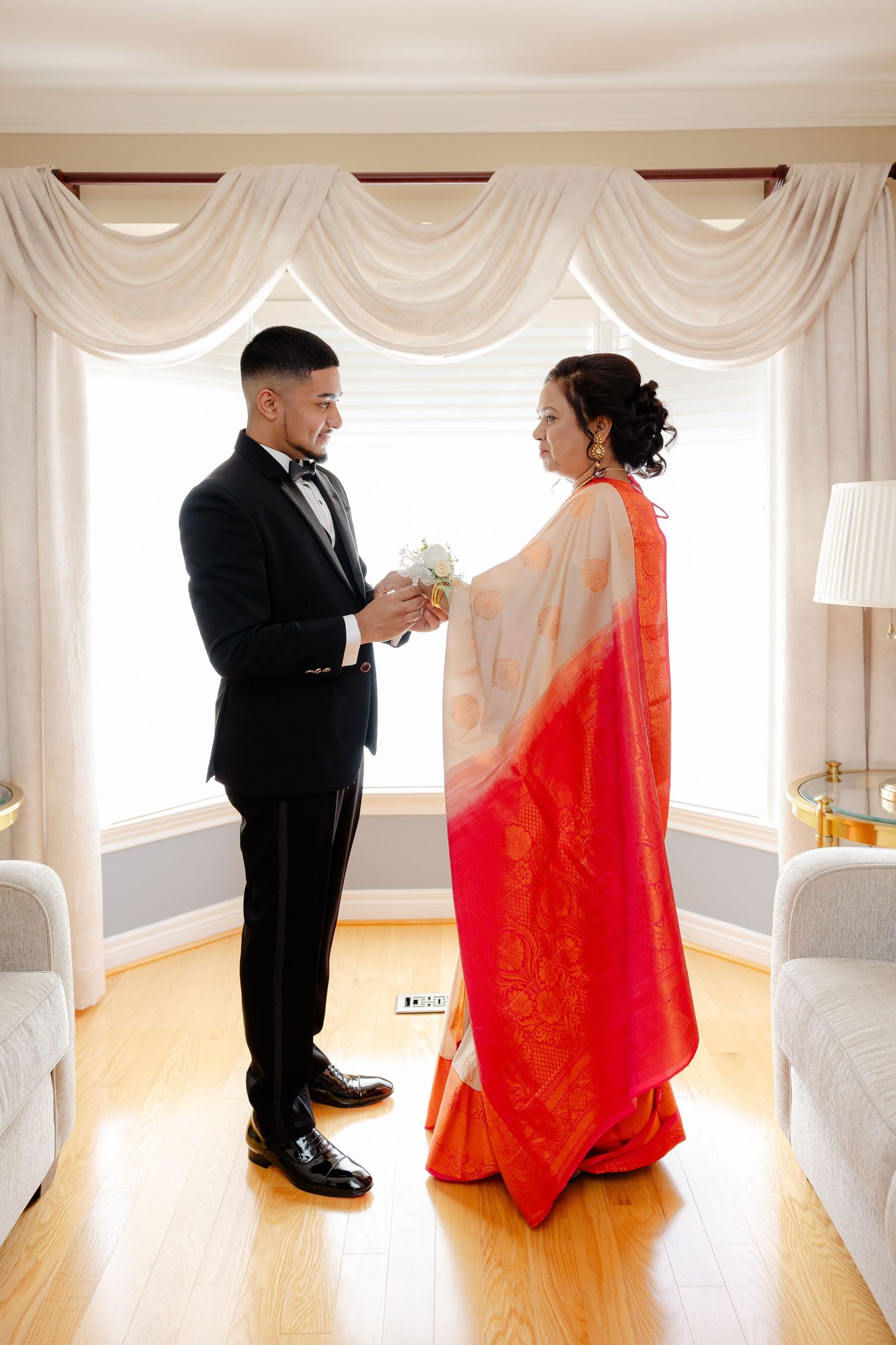 Wedding ceremony couple in traditional dress exchanging rings in elegant room with draped windows.