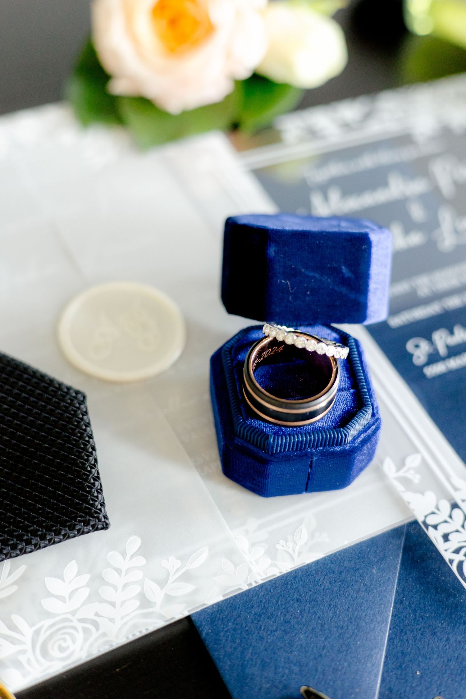 Wedding rings displayed in navy velvet ring box with invitation suite and floral details.