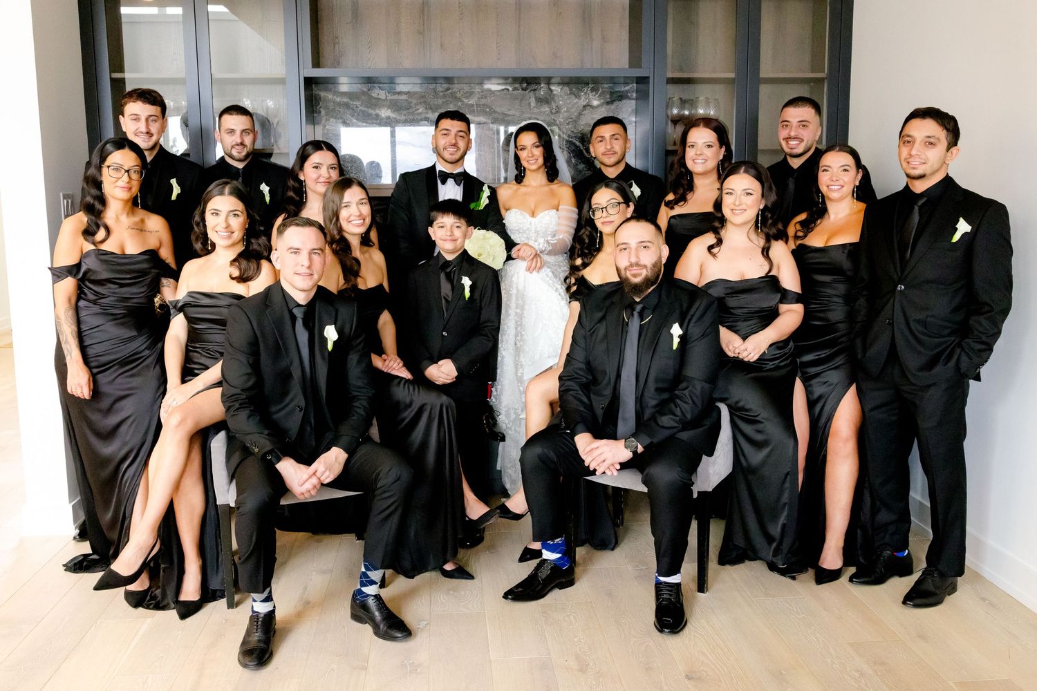 Wedding party members in elegant black attire gather for a formal group photograph.
