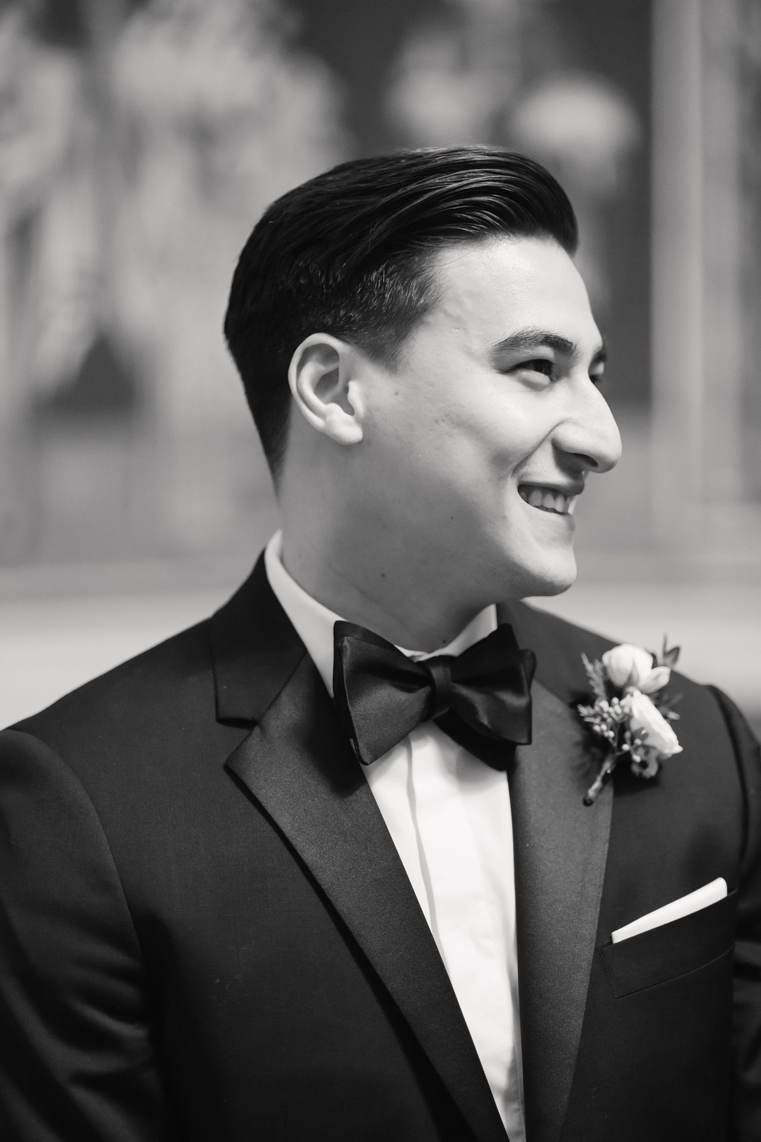 Profile portrait of a groom in black tuxedo and bowtie smiling with boutonniere.