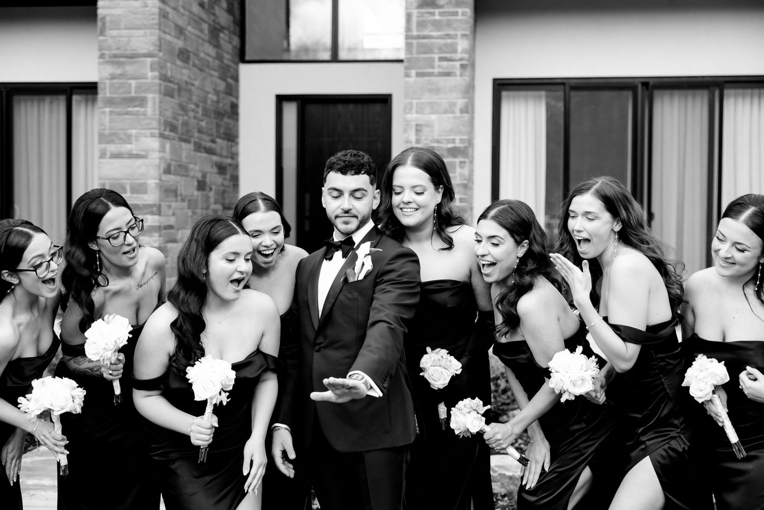 Wedding party in black attire shares candid laughing moment together outdoors.