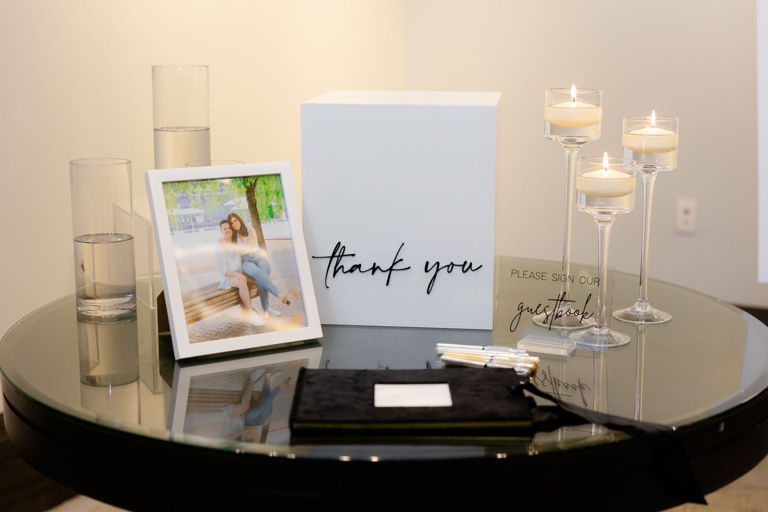 Wedding reception guest book table with thank you sign, photo frame, and floating candles.