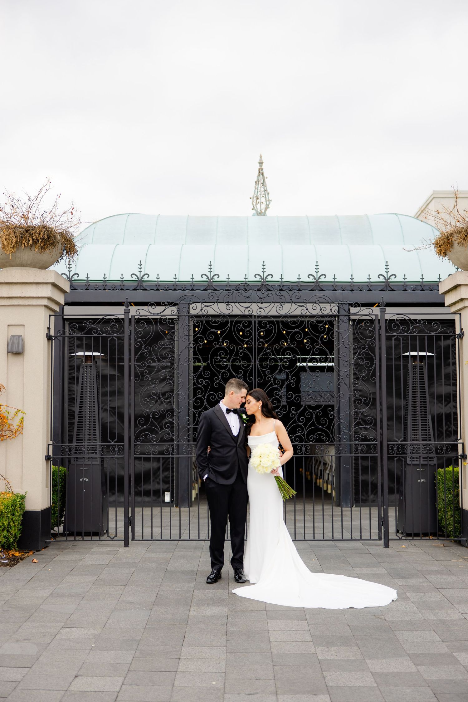 Romantic wedding portrait in front of ornate black gates and classical architecture.