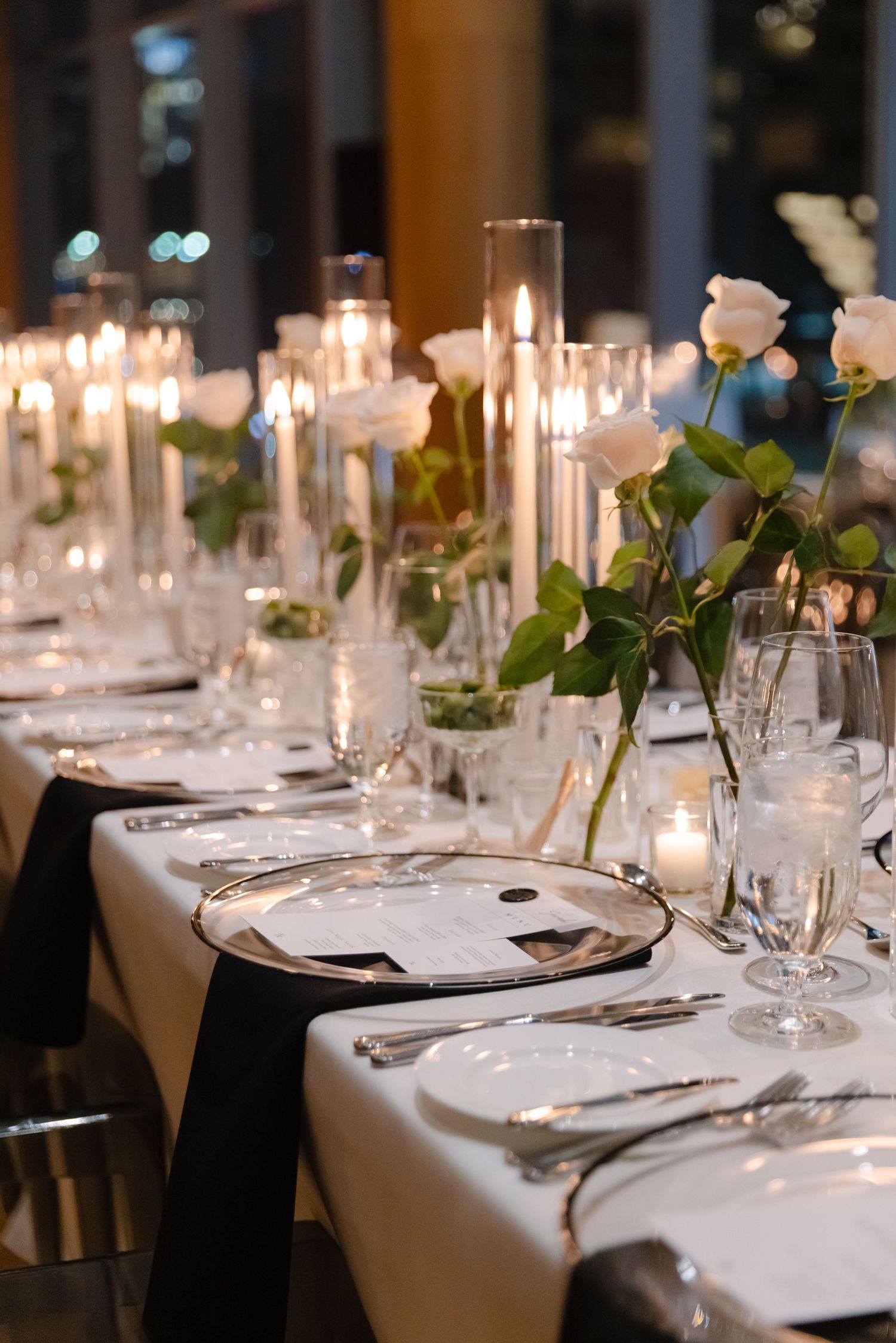 Formal dining table with black napkins, white roses, and glowing candlelight.