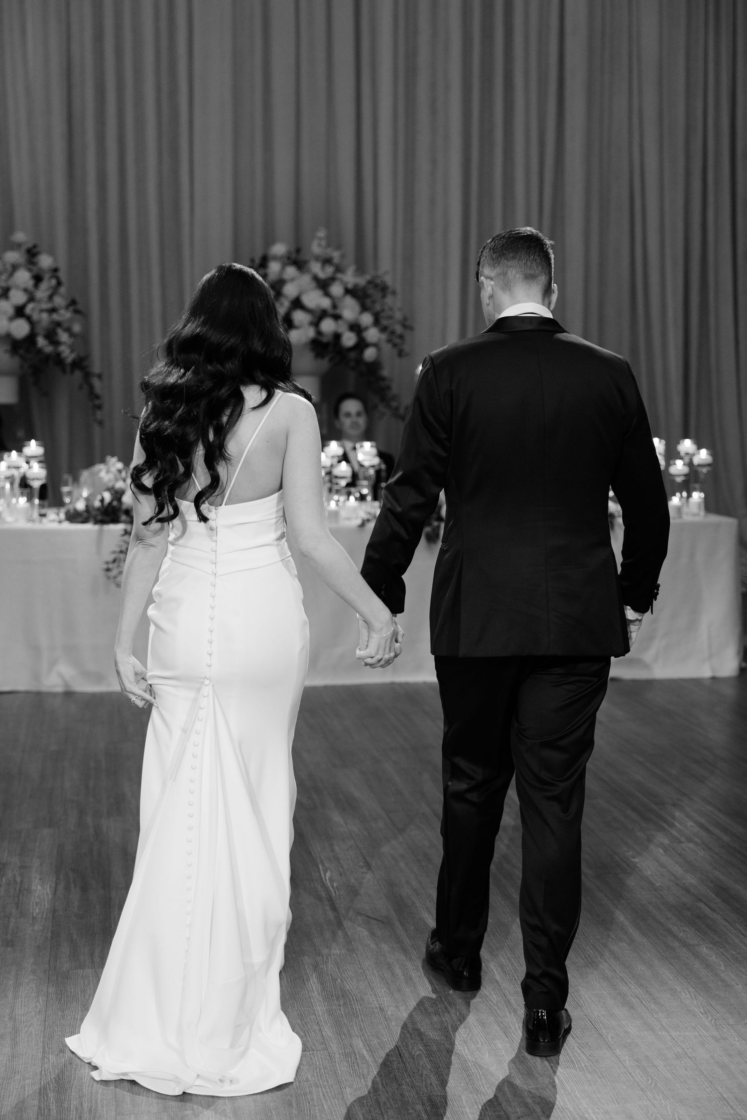 Back view of a couple walking across their wedding reception dance floor.