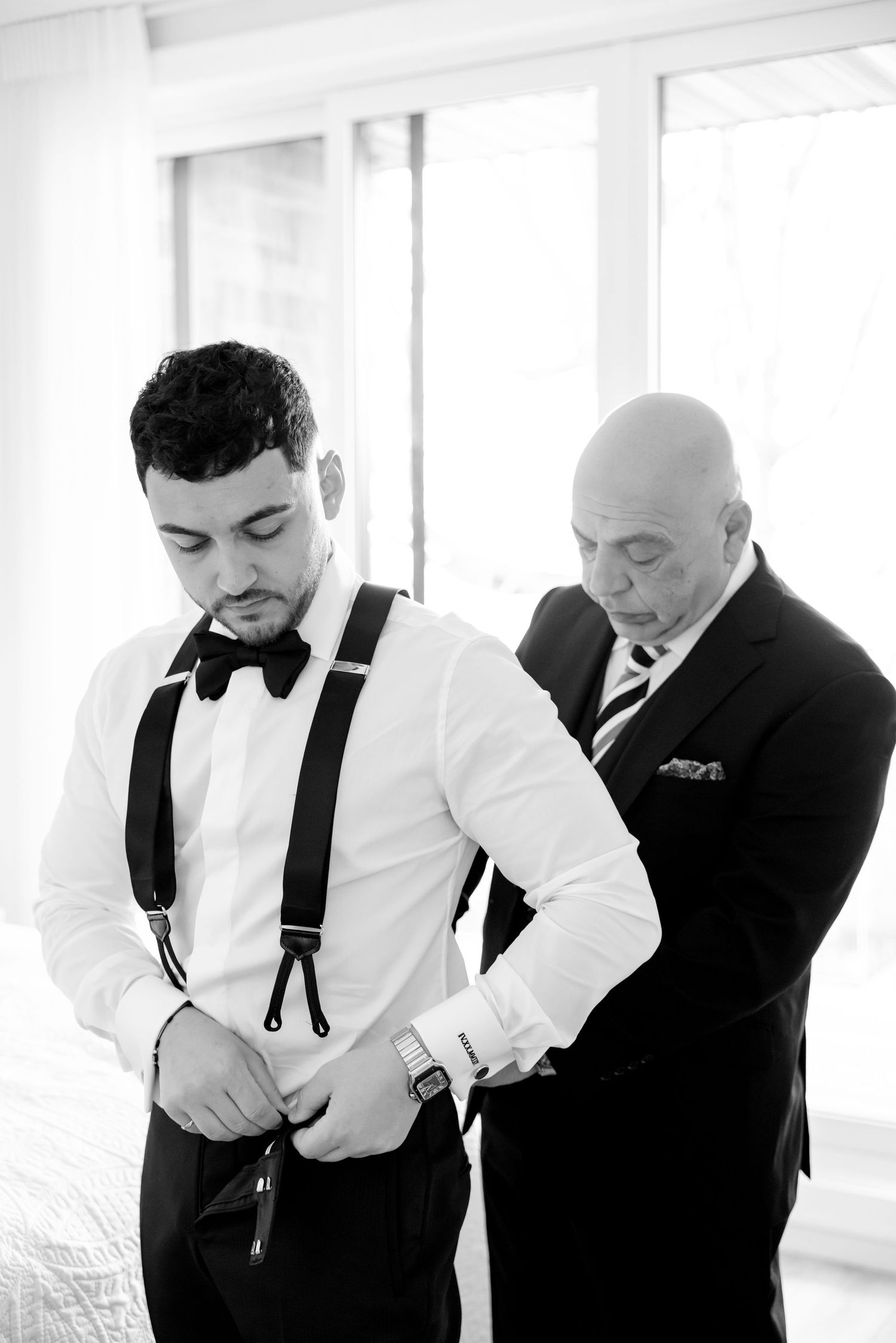 Black and white photo of wedding preparations with formal attire and suspenders.