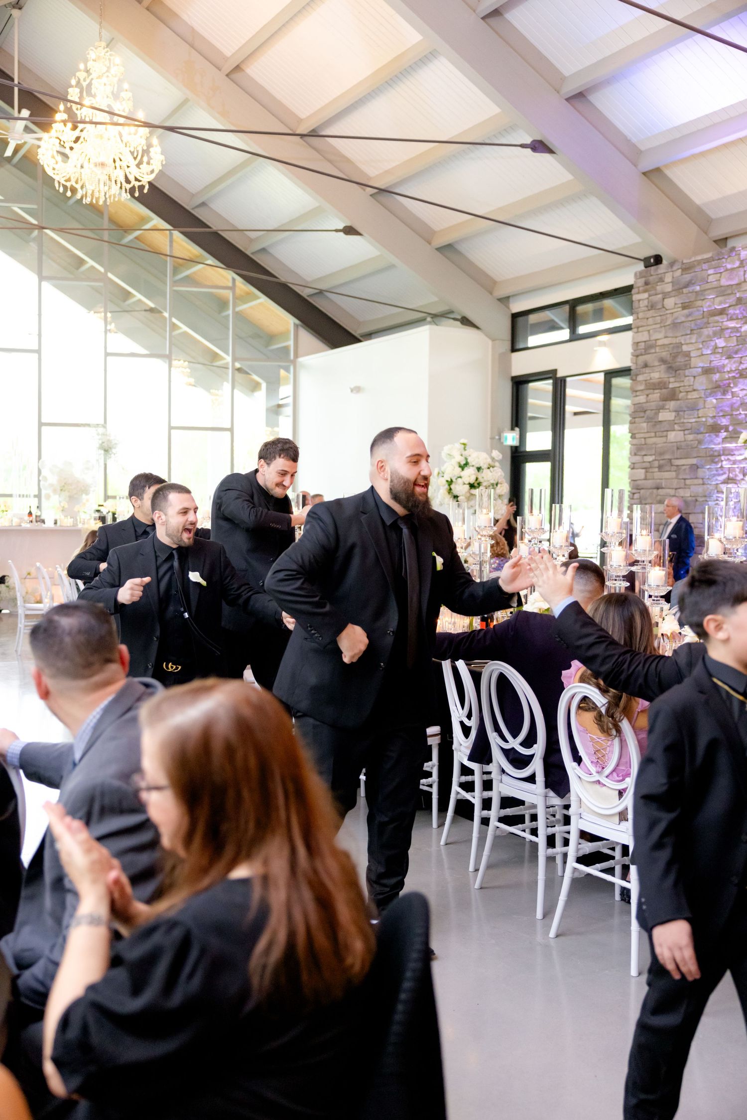 Celebratory scene at a modern wedding reception with white chairs and vaulted ceilings.