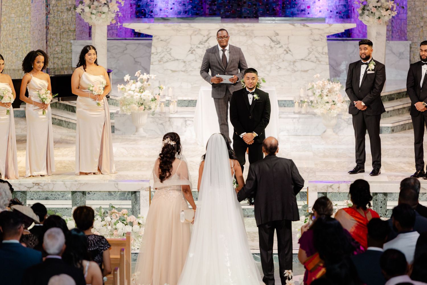 Wedding ceremony view from back of church showing decorated altar and gathered guests.