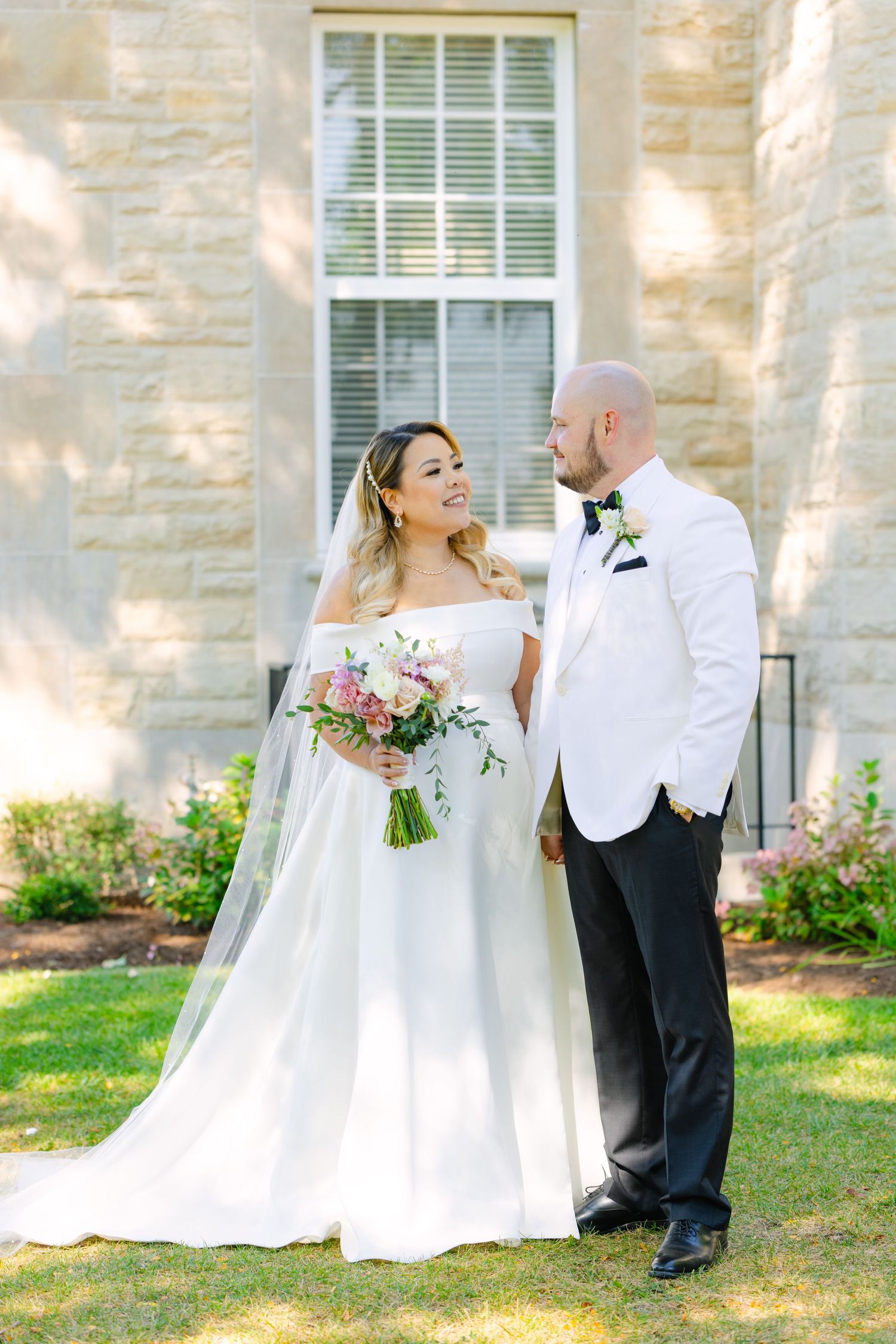 The newlyweds share a happy moment together on the lawn of a historic stone building.