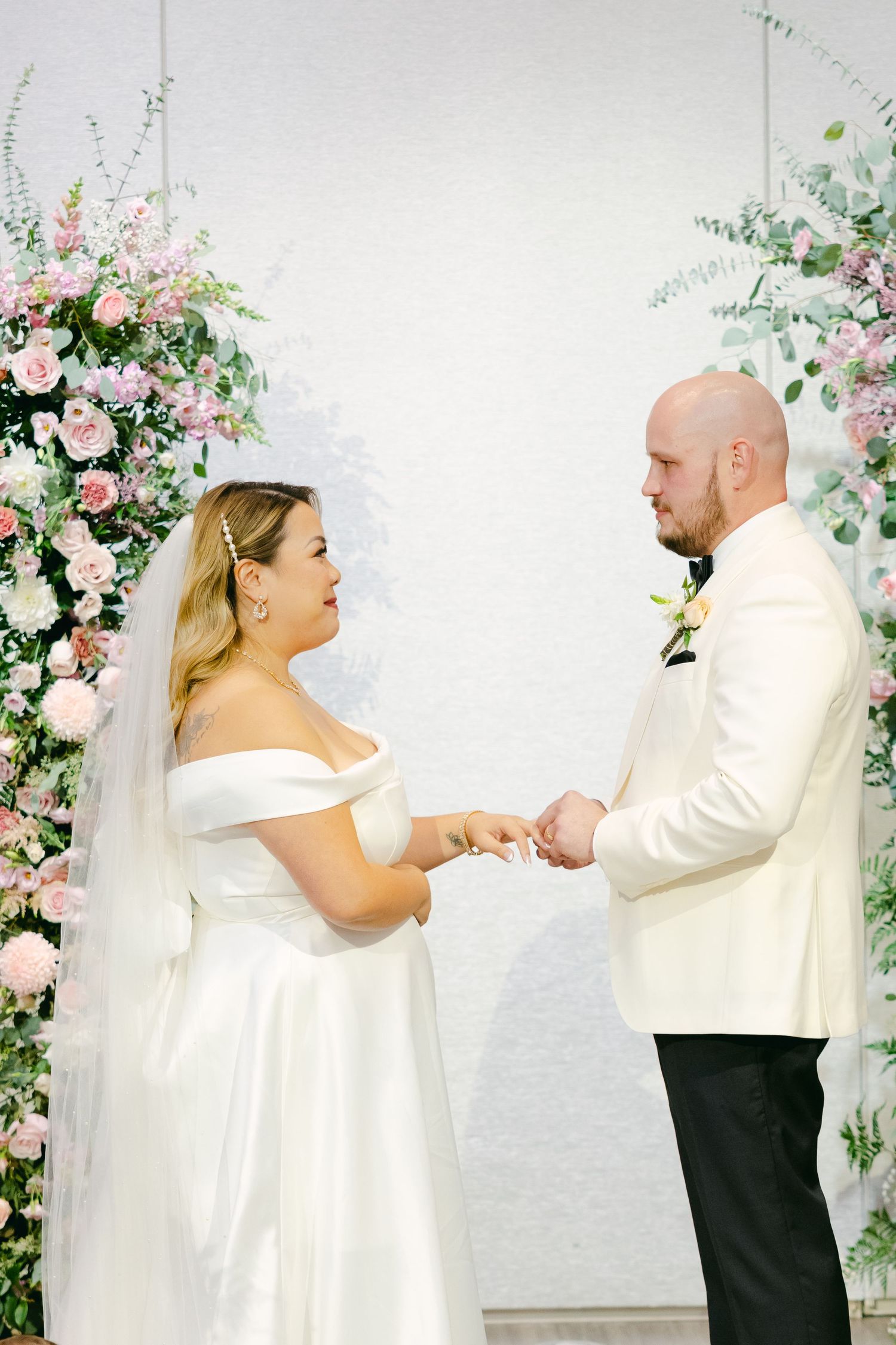 Elegant wedding ceremony with couple exchanging rings under rose-adorned floral arches.