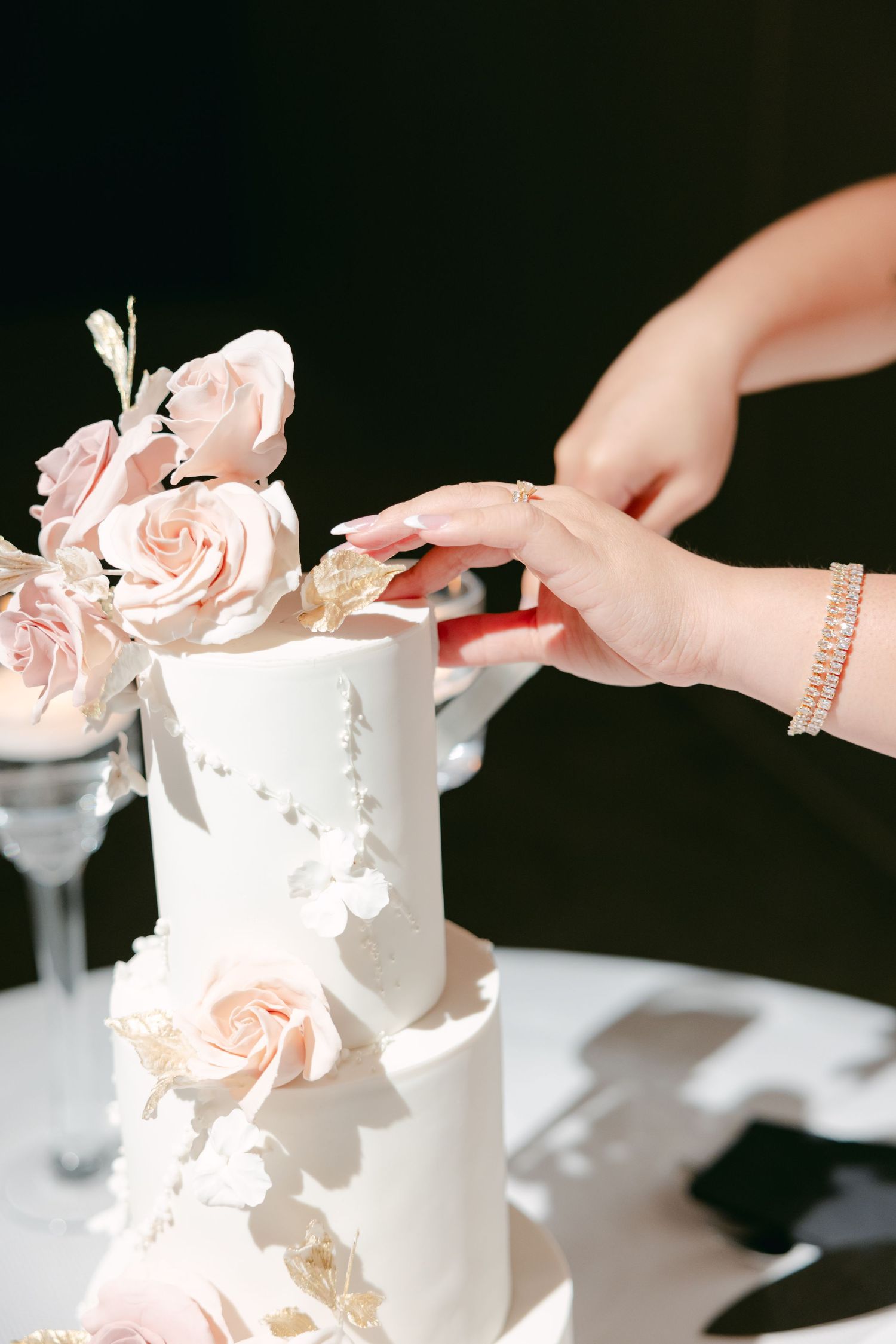 Close-up of hand touching white wedding cake decorated with delicate pink roses.