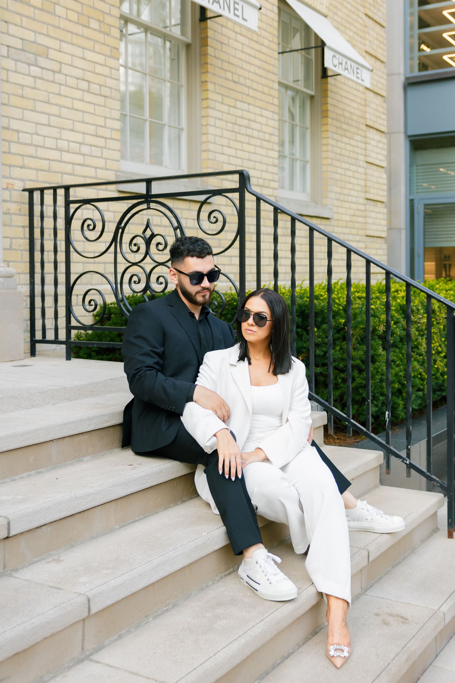 Modern couple in black and white attire sitting casually on stone steps outside Chanel.