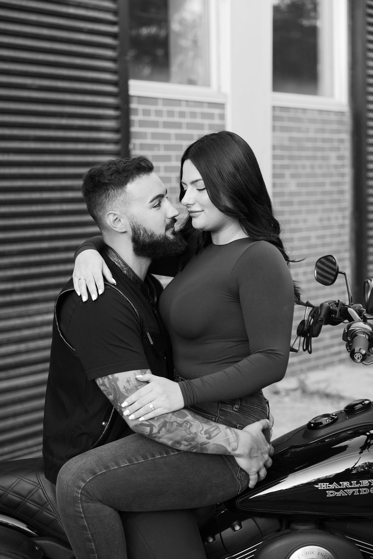 An intimate black and white portrait captures a couple's tender moment on a motorcycle.