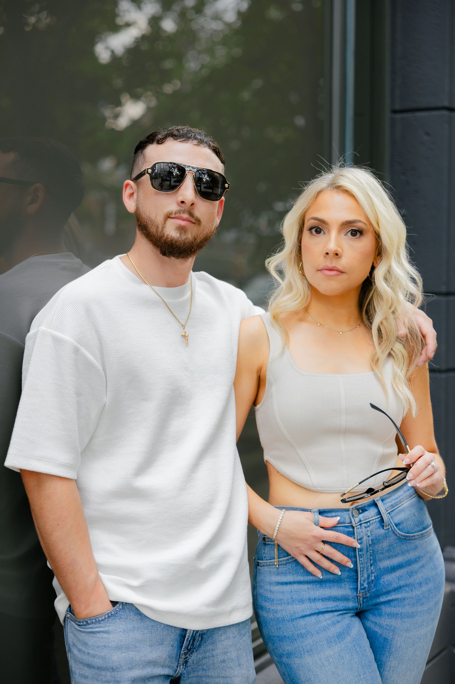 A stylish couple in coordinated white and denim outfits pose outdoors.