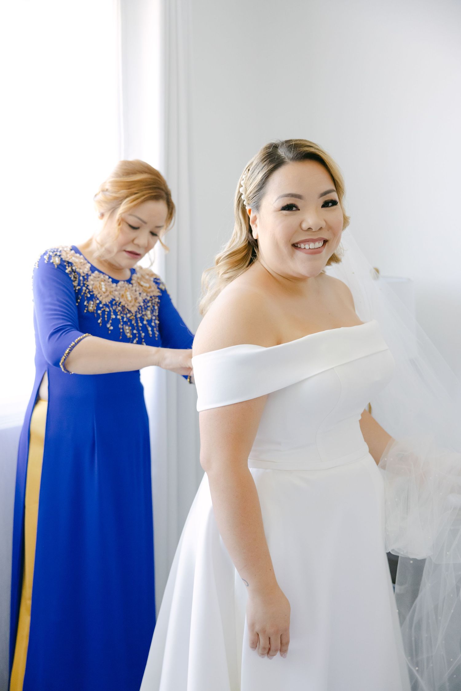 A helper in royal blue adjusts a white wedding dress during final preparation moments.
