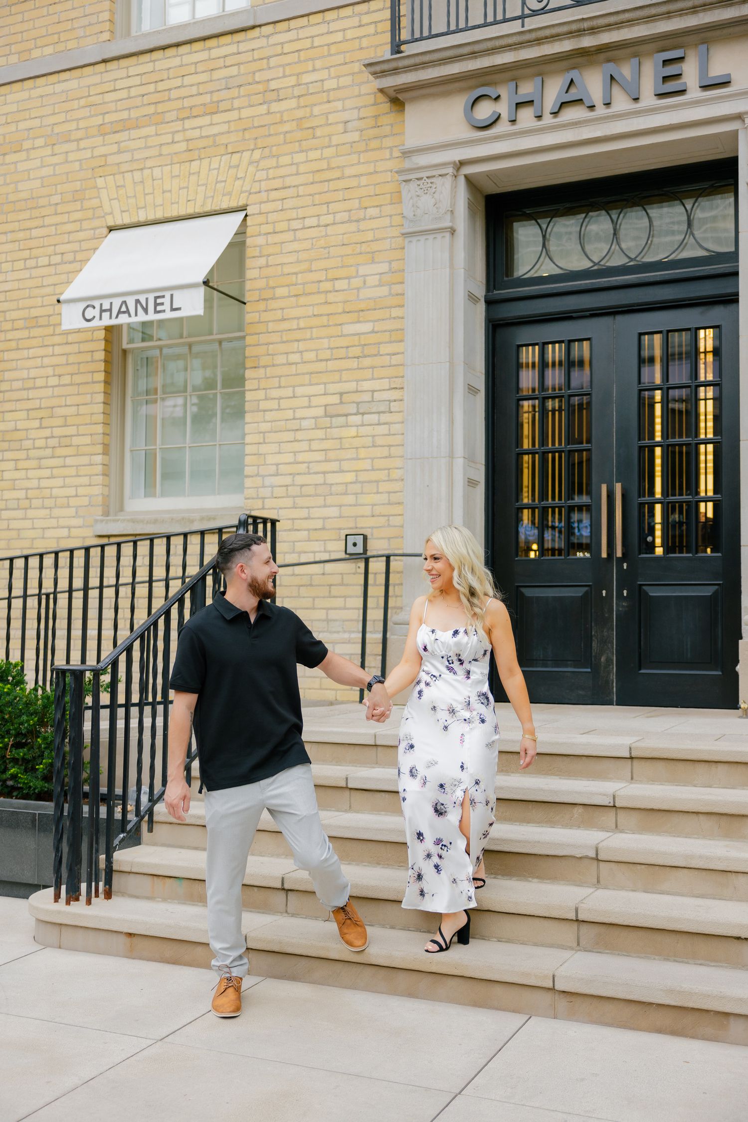 Couple holds hands while descending Chanel store steps in stylish attire.
