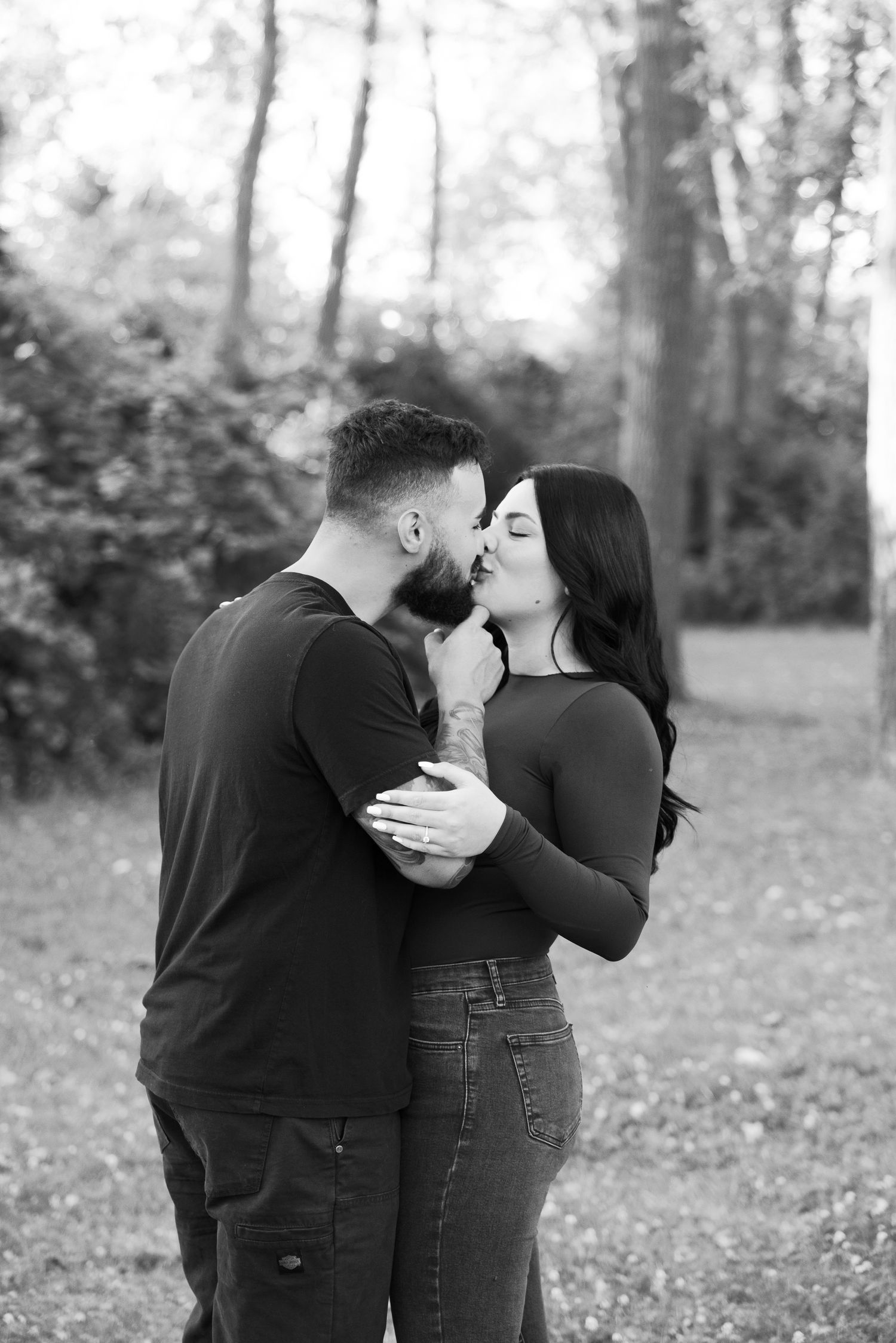 Romantic couple sharing an intimate moment in a forest setting, captured in black and white.