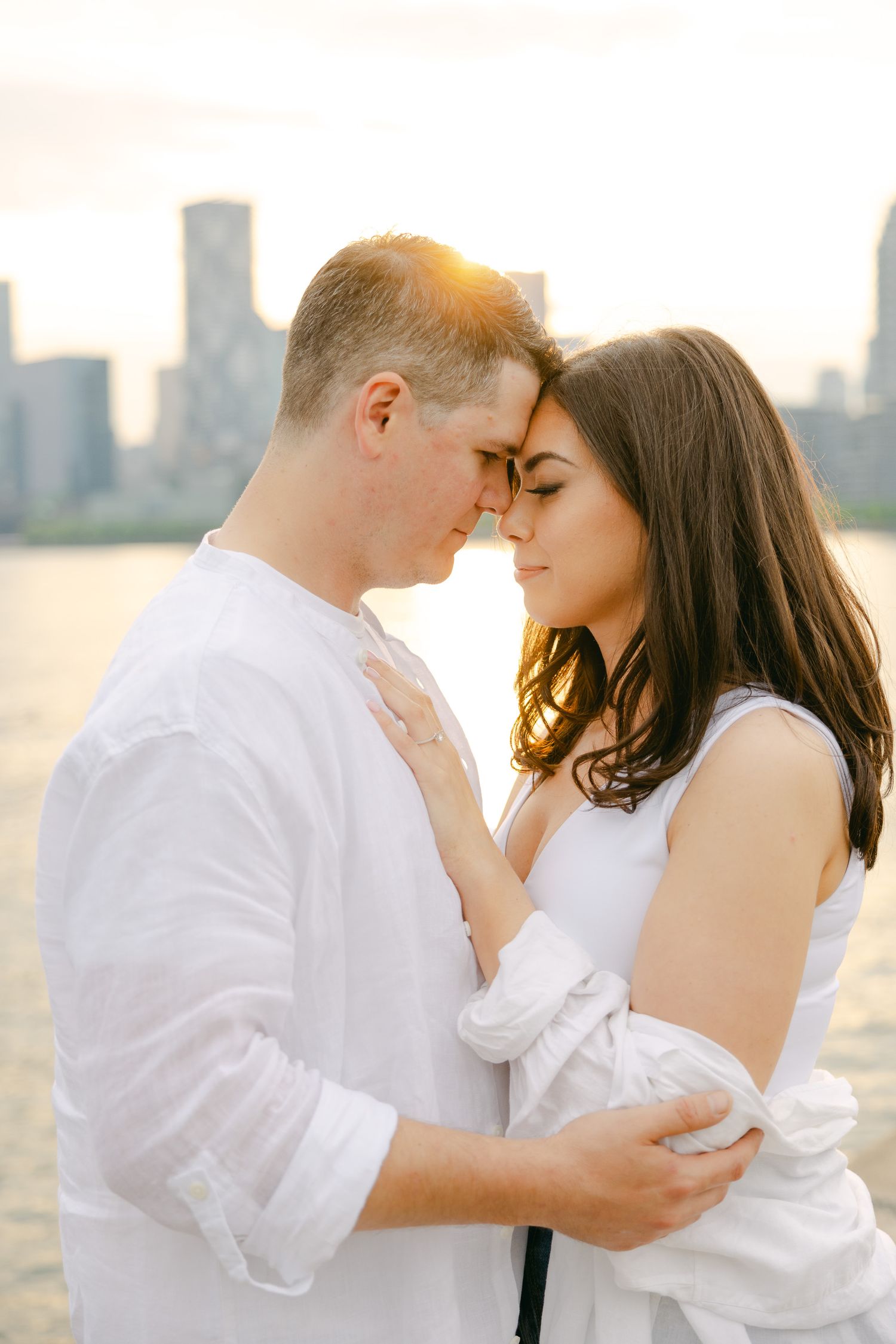 A romantic sunset engagement photo showing a couple in white sharing an intimate moment.
