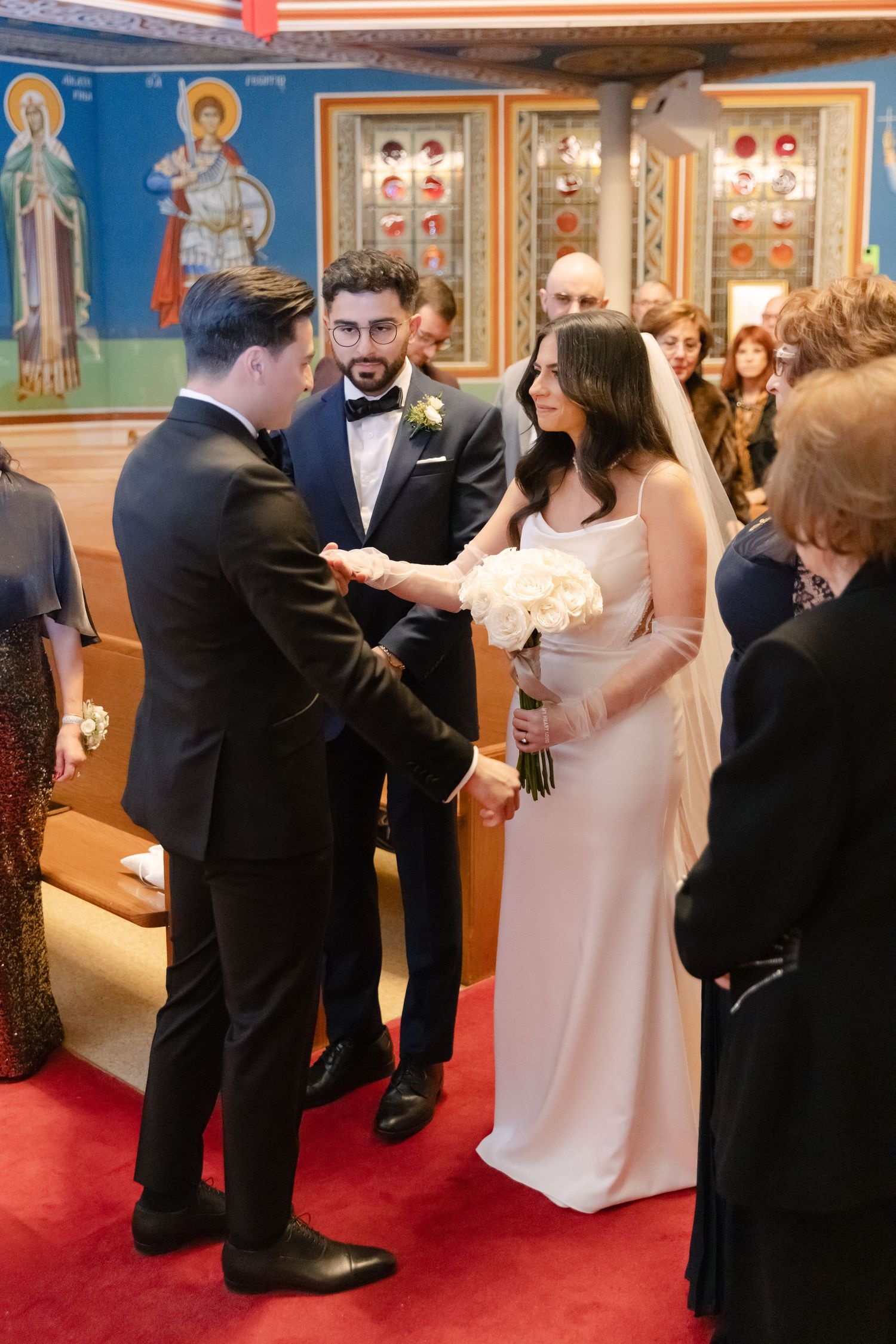 Wedding ceremony moment in church with religious artwork and stained glass windows.