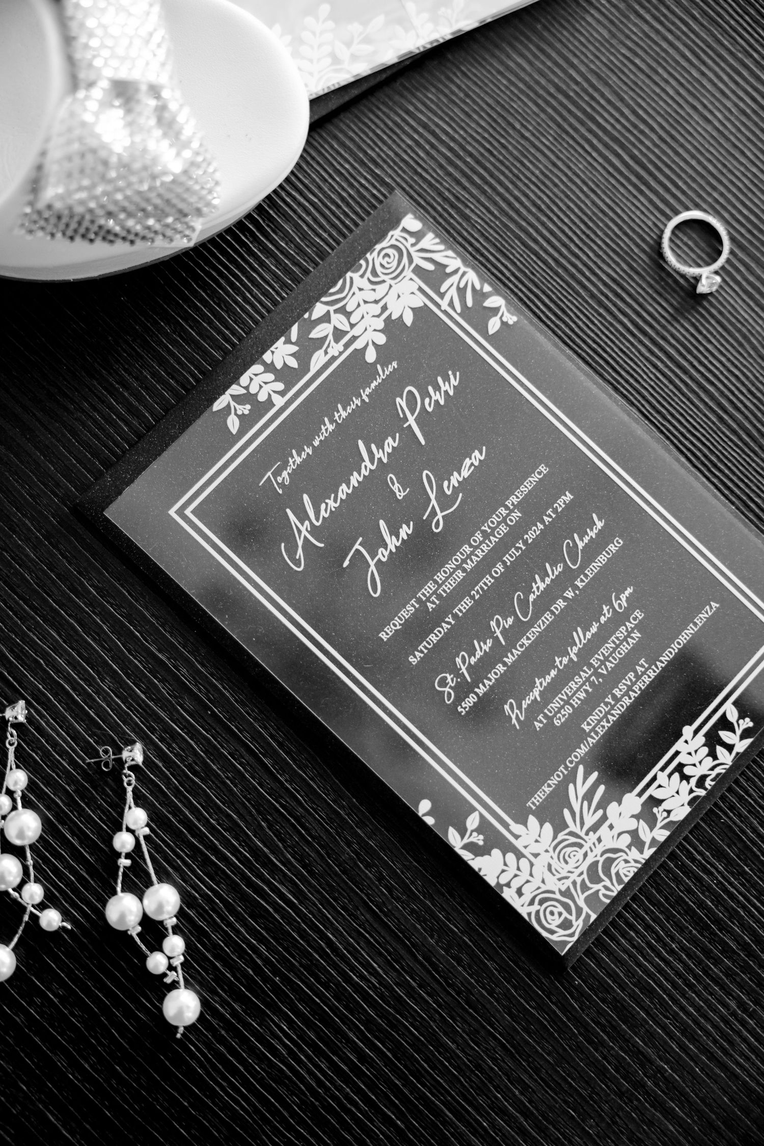 Black and white wedding invitation with elegant floral border design and pearl earrings.