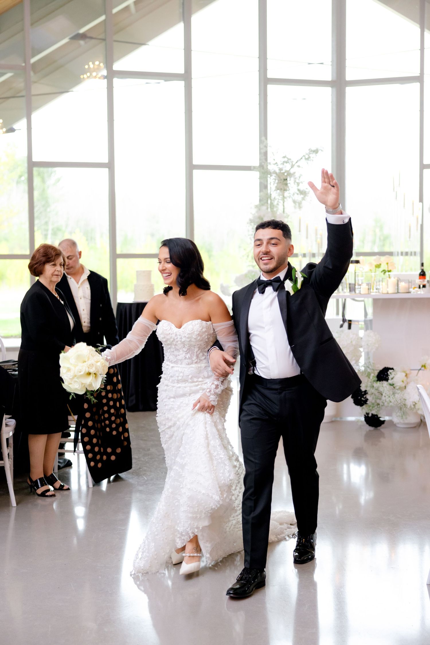 Newlyweds celebrate during their reception entrance in a modern white venue with large windows.