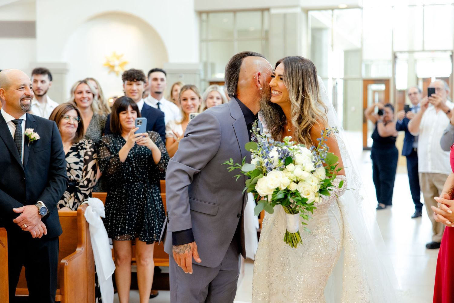A romantic moment during a wedding ceremony with guests watching in a bright indoor venue.