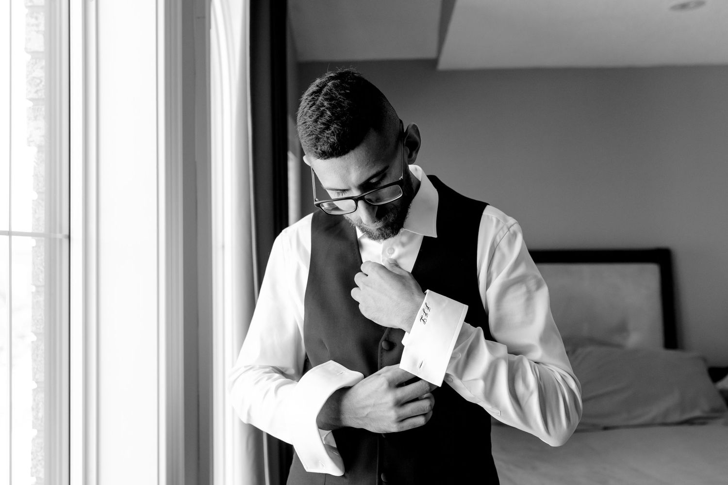 A person in formal attire adjusts their cufflinks while standing by a window.