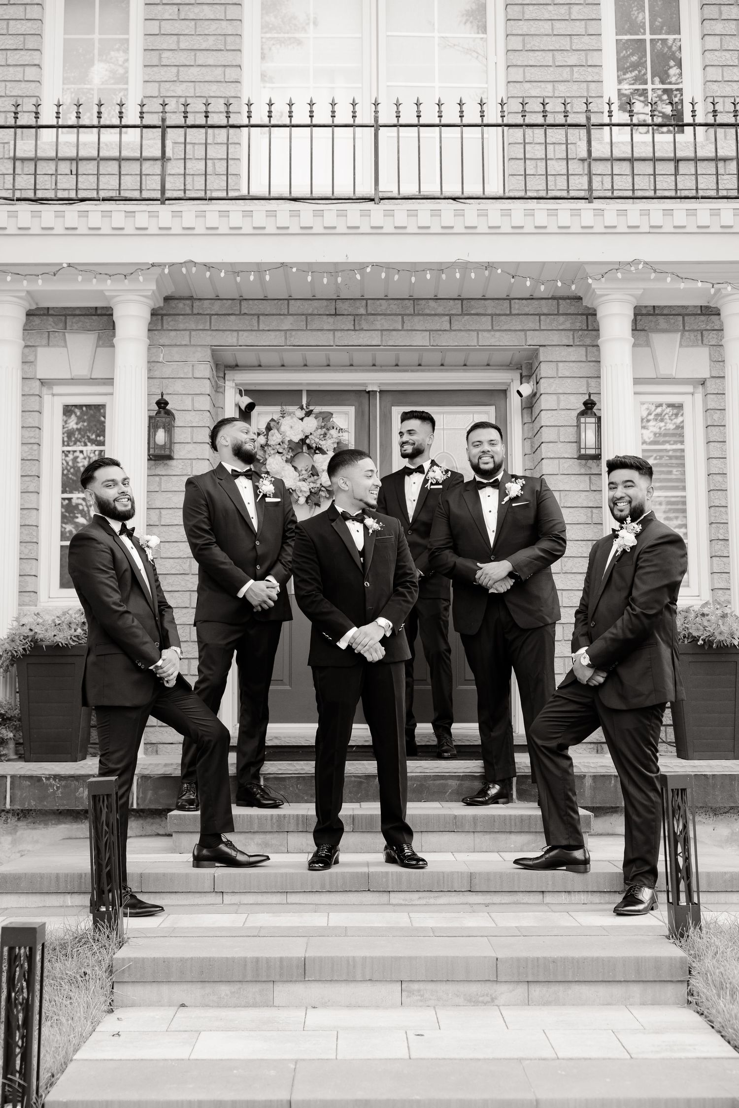 Black and white portrait of groomsmen group gathered on classic mansion entrance steps.
