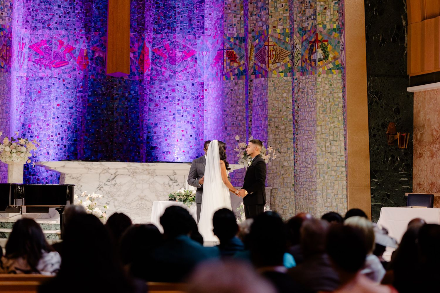 Silhouetted wedding ceremony against purple-lit backdrop with crowd watching from below.