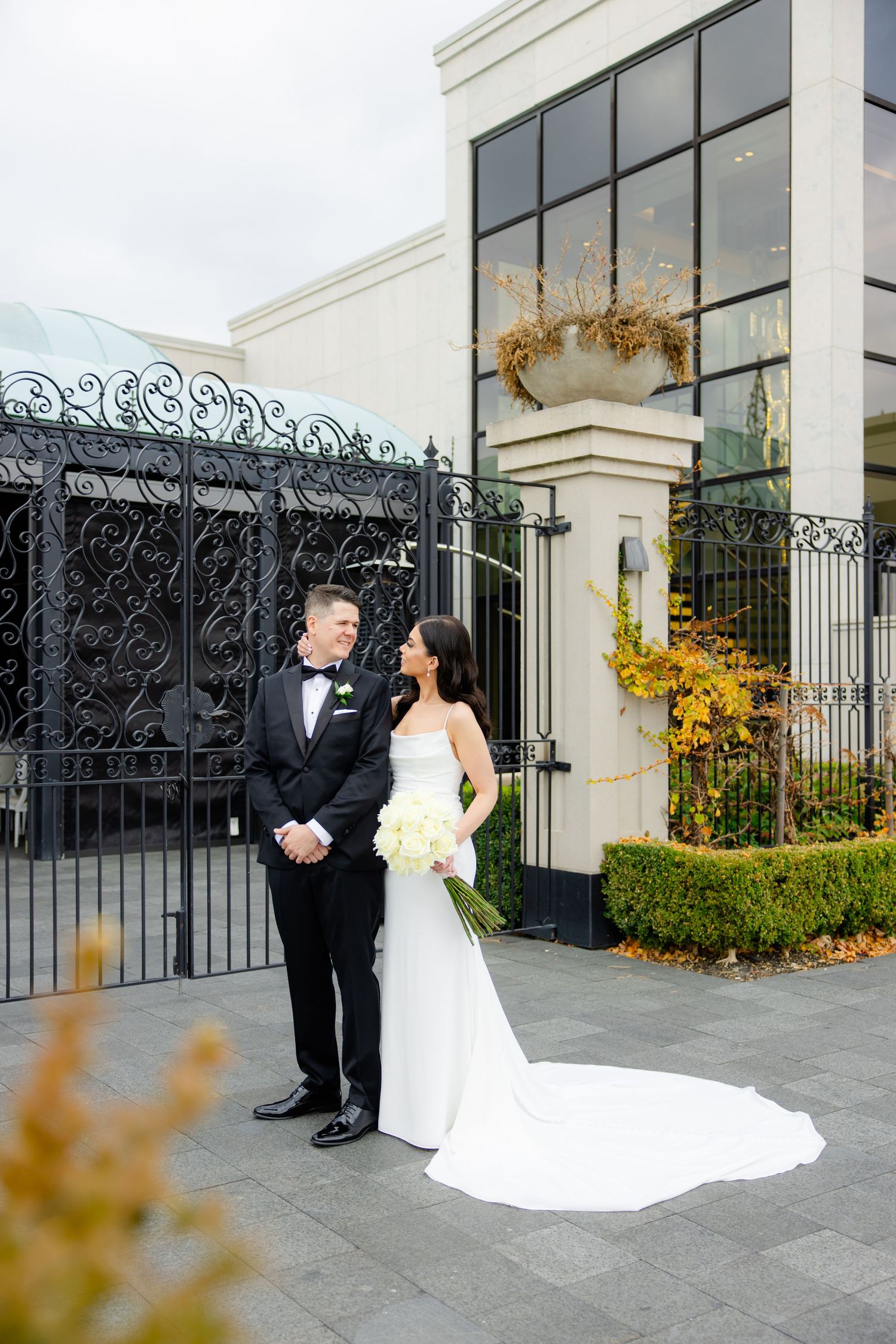 Modern wedding portrait with couple standing by black gates and contemporary building facade.